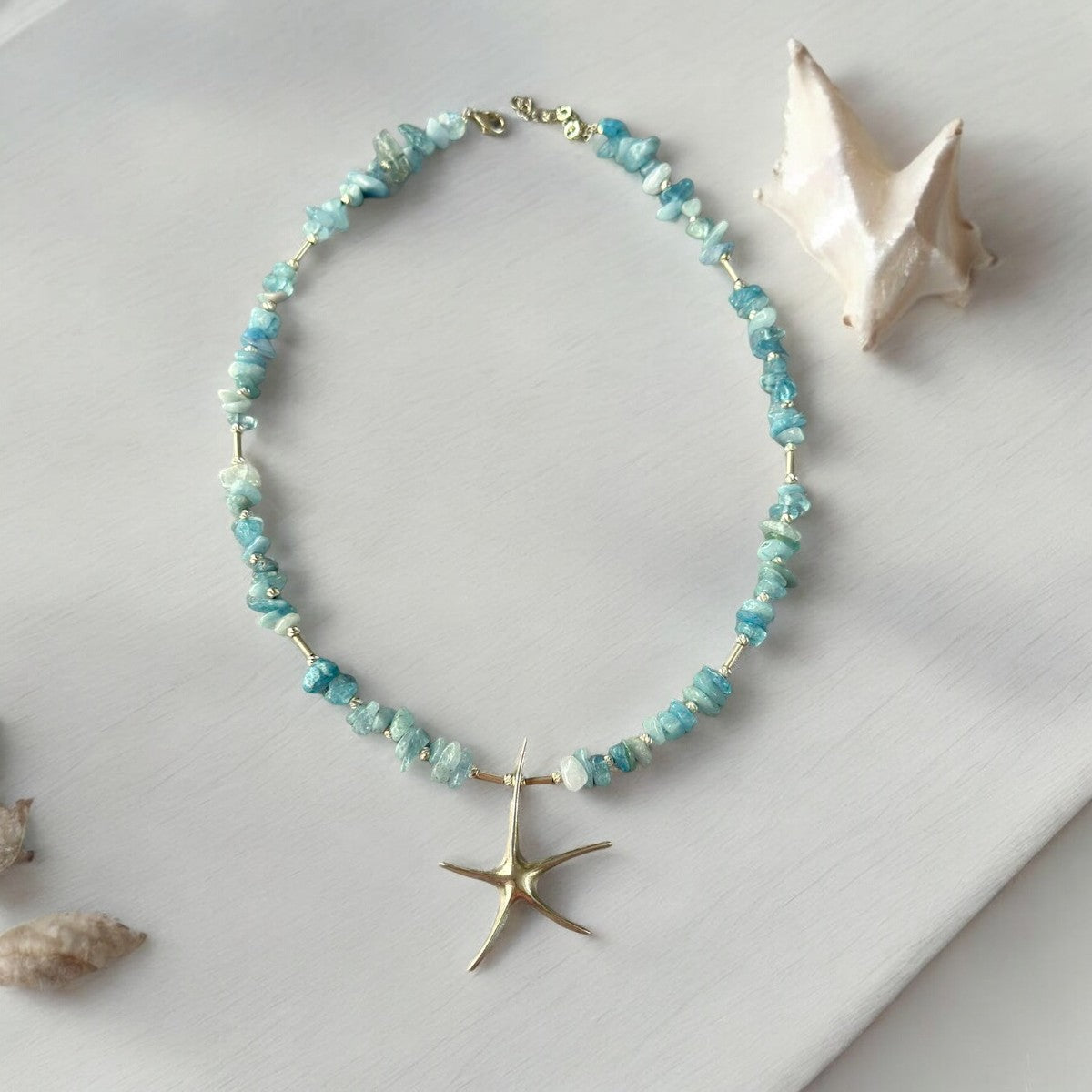 Handmade Aquamarine Starfish Necklace in 925 Silver displayed elegantly with seashell background