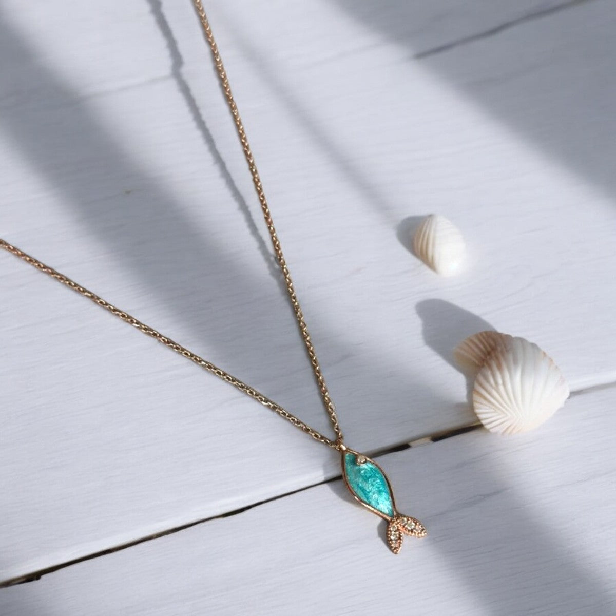 Azure Silver Fish Necklace - Handcrafted Rose Gold Plated displayed on white wooden surface with seashells