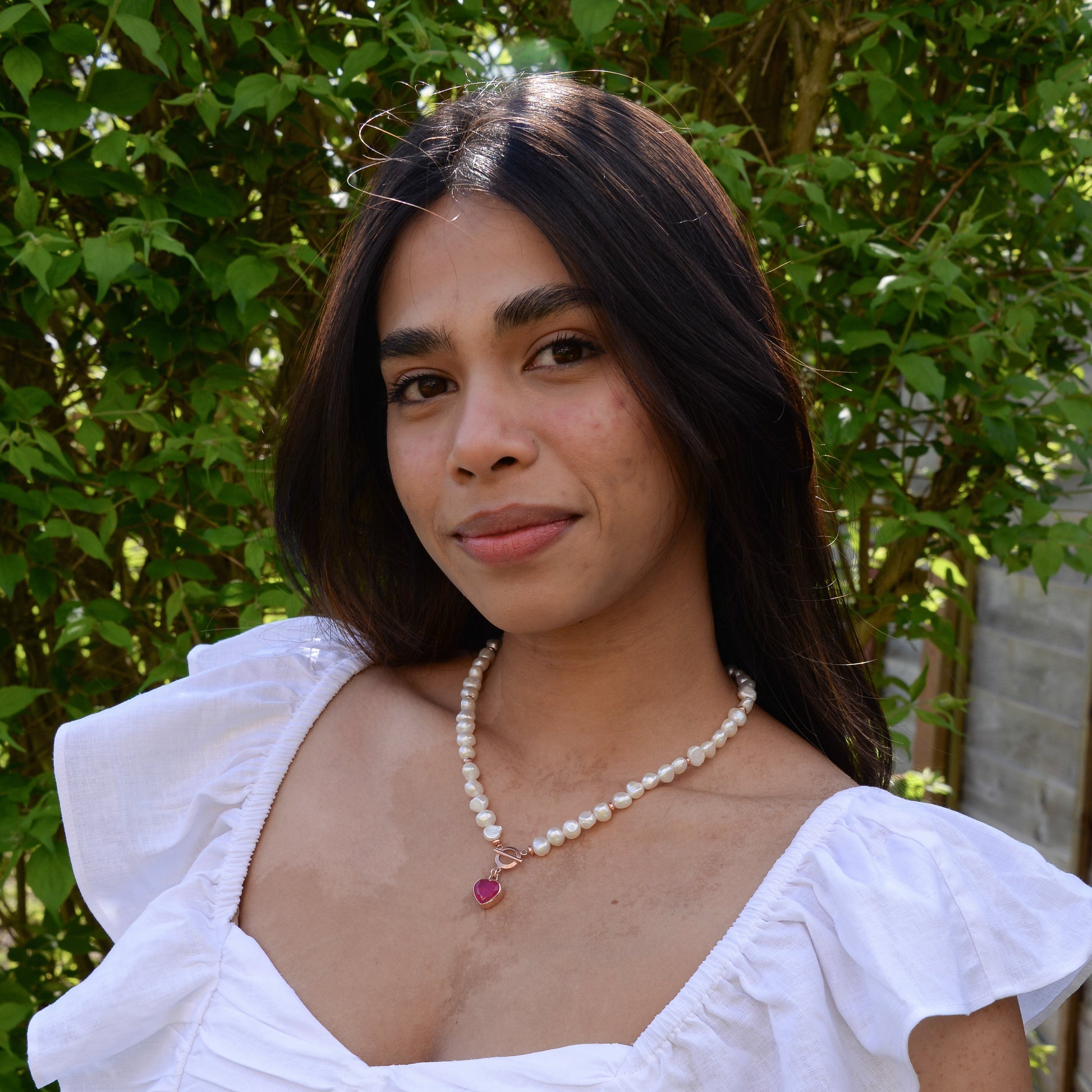 Woman wearing Baroque Pearl Heart Necklace with white blouse and green foliage background