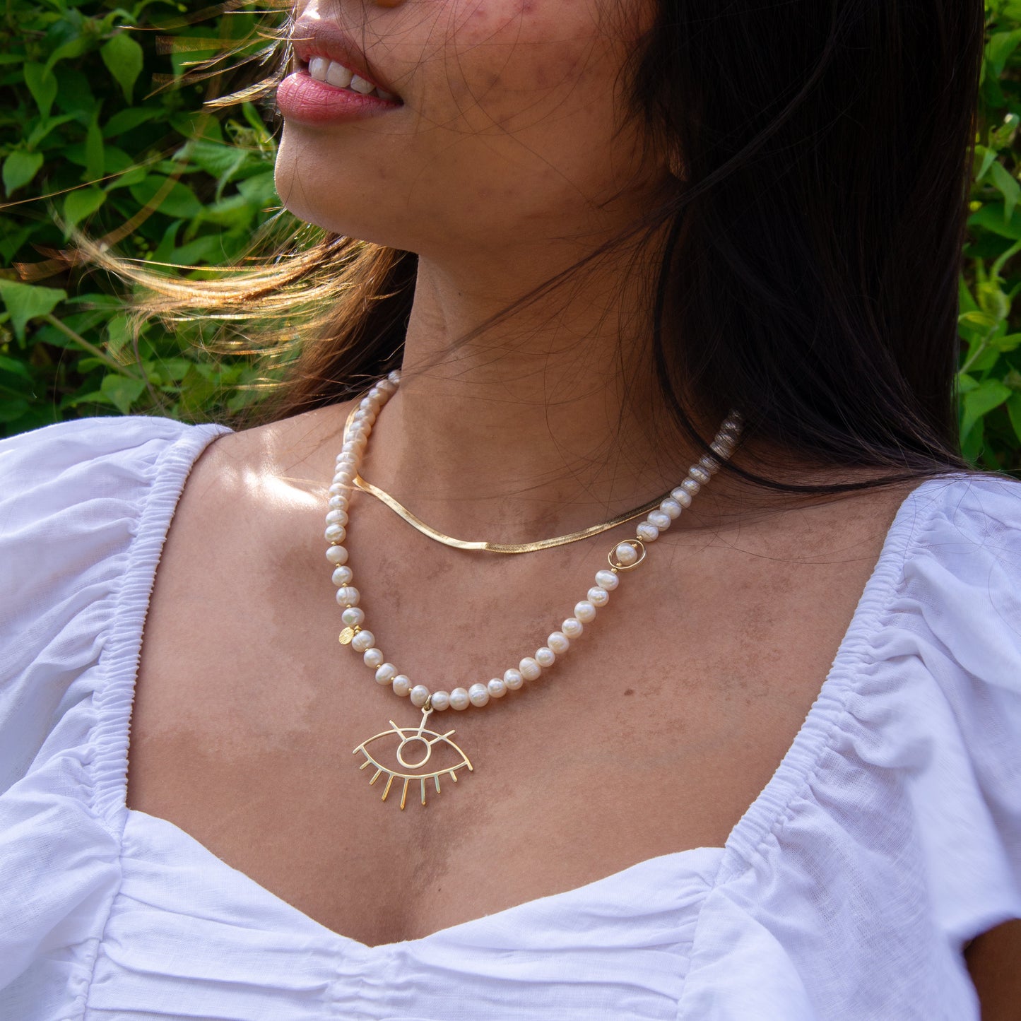 Baroque Pearl Silver Eye Necklace worn by a woman in a white dress, shown outdoors with green foliage background.