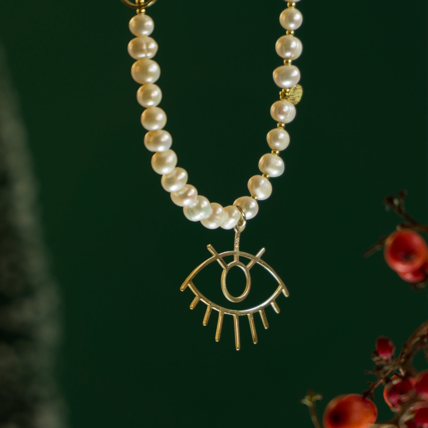 Baroque Pearl Silver Eye Necklace with intricate eye pendant on a string of pearls, against a dark green background.