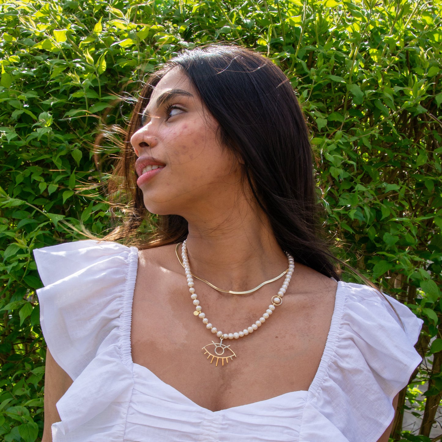 Woman wearing Baroque Pearl Silver Eye Necklace in front of lush green bush.