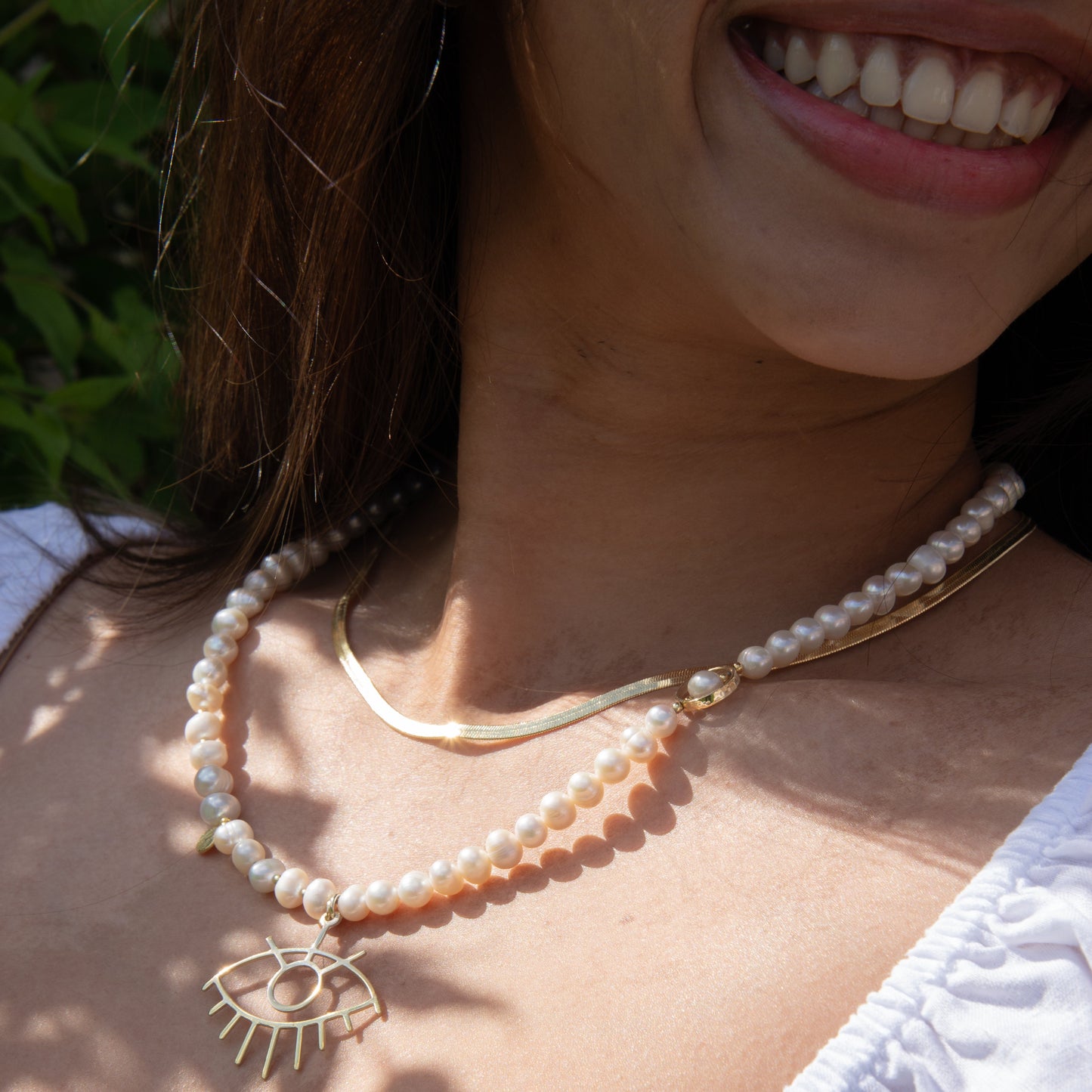 Woman wearing a Baroque Pearl Silver Eye Necklace with gleaming pearls and a unique eye pendant, in an outdoor setting.