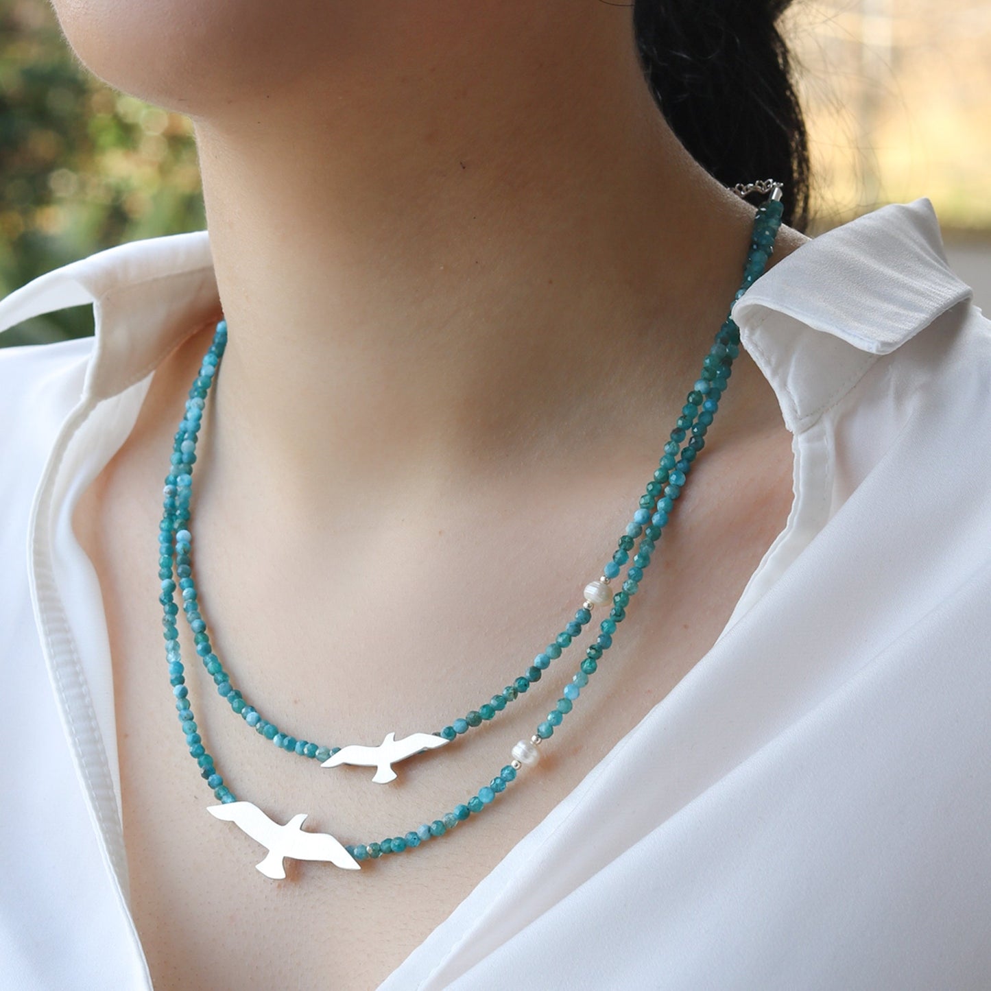 Close-up of Big and Small Seagull Apatite Silver Necklace on woman's neck wearing a white shirt.