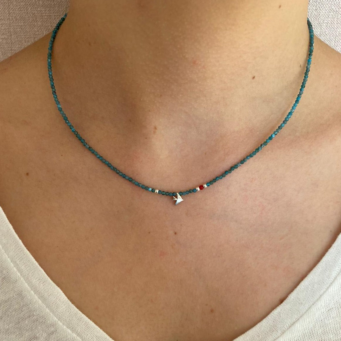 Woman wearing Birdie Minimal Silver Necklace with blue beads and small bird charm.