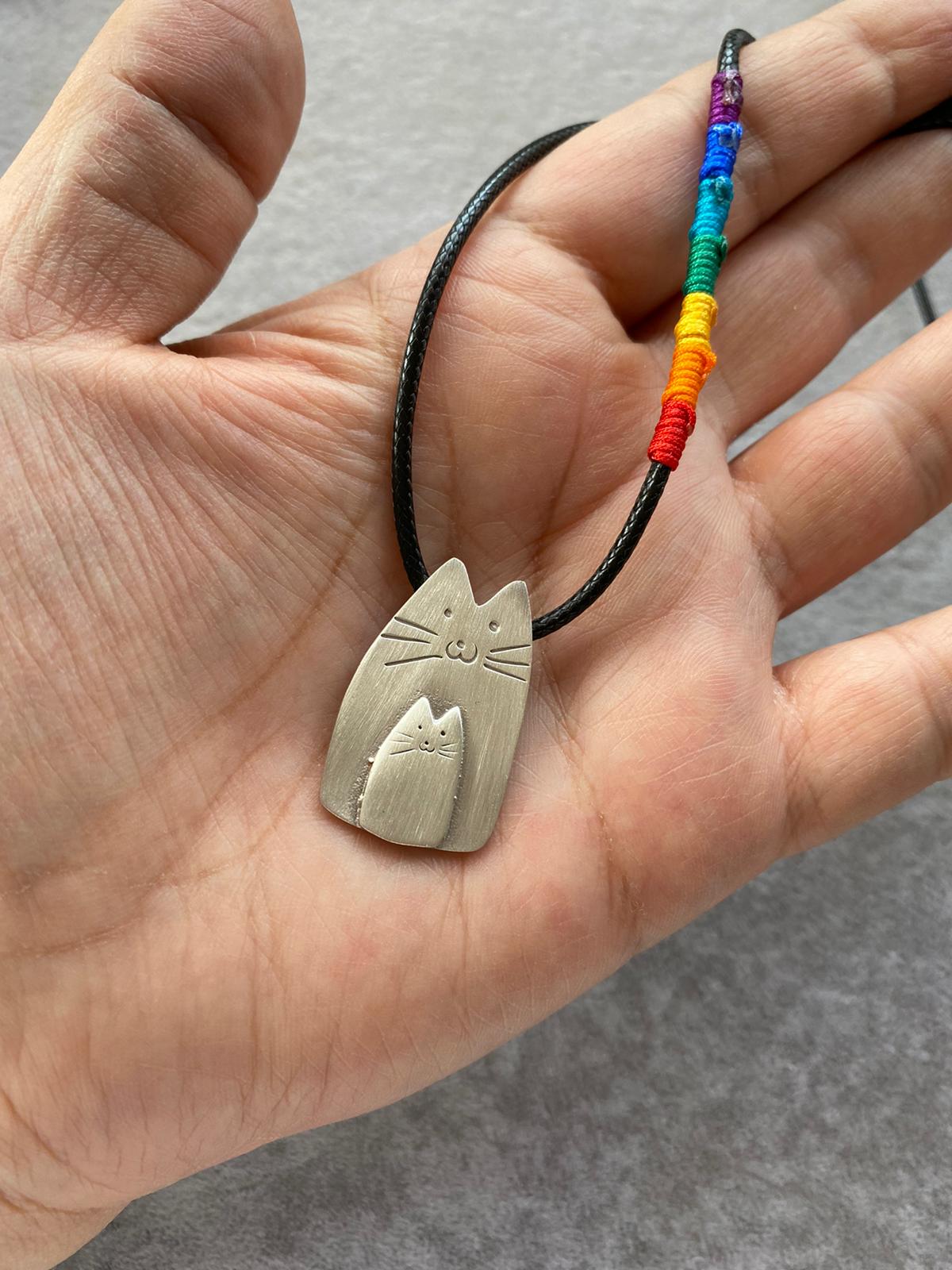 Hand holding a Cutie Cat Silver Necklace with rainbow-accented cord