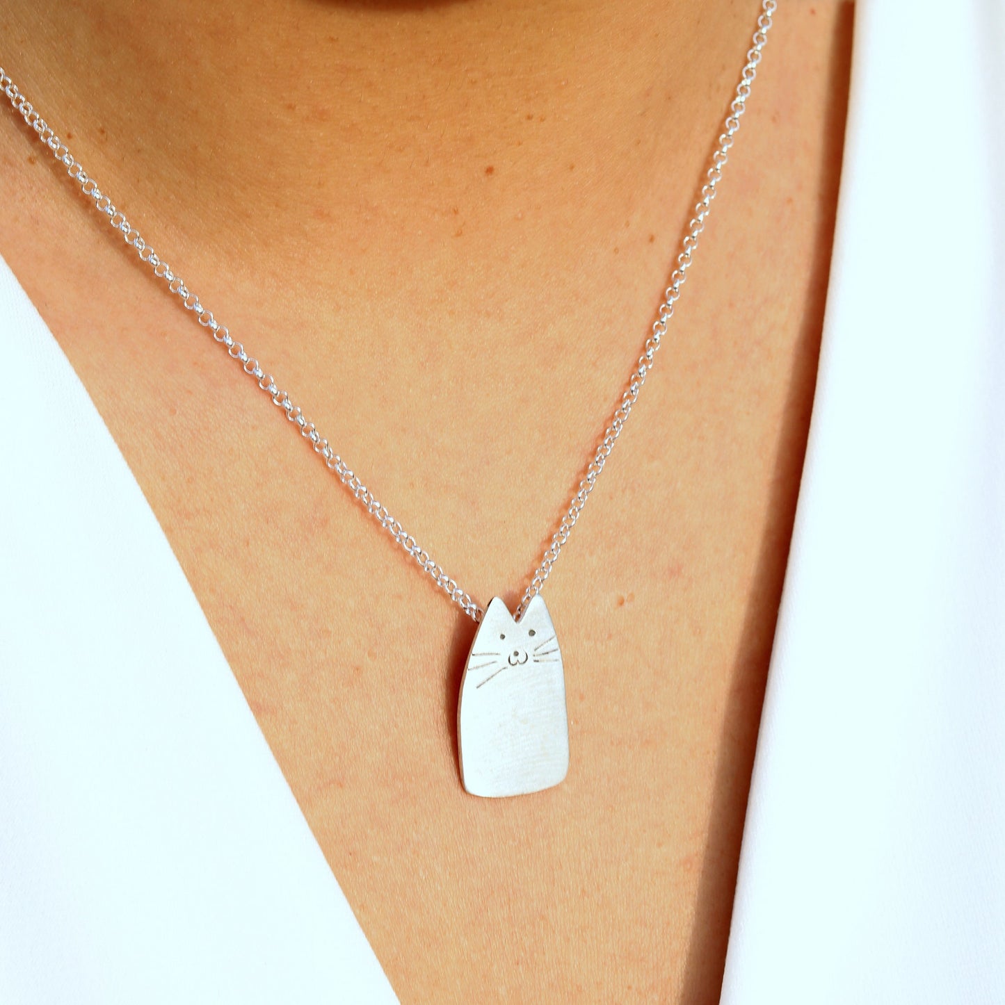 Cutie Cat Silver Necklace elegantly worn on a person with a white top.