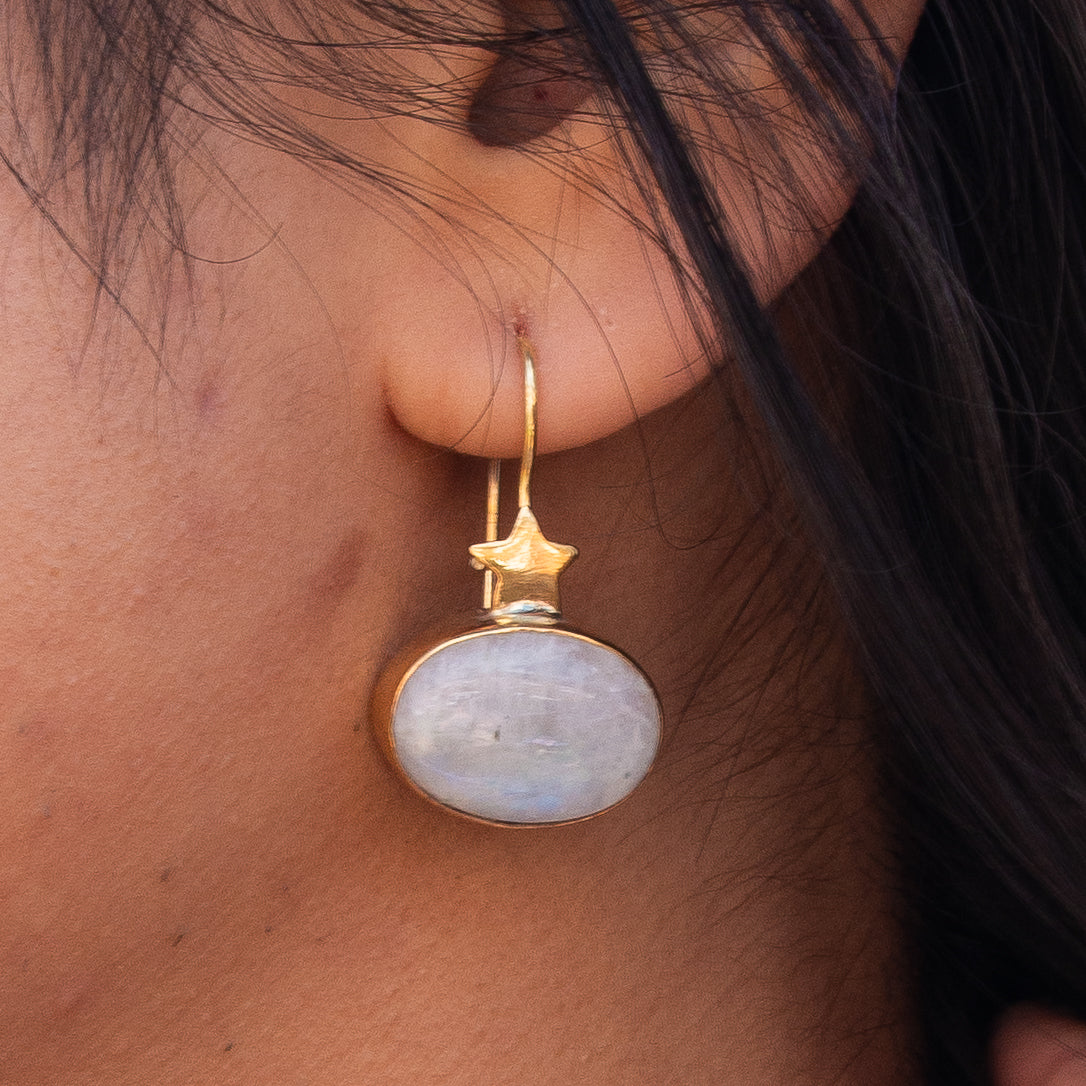 Day and Night Moonstone Silver Necklace on woman’s ear, featuring a star-shaped gold accent and a luminous moonstone pendant.