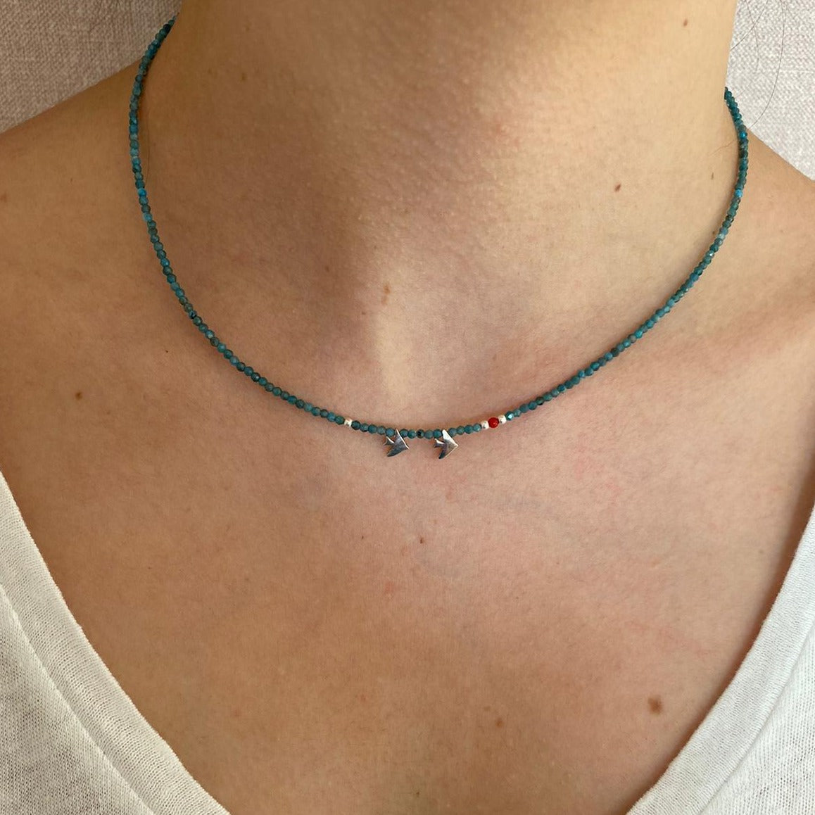 Close-up shot of Duo Birdie Minimal Silver Necklace on a woman's neck with teal beads and small bird charms