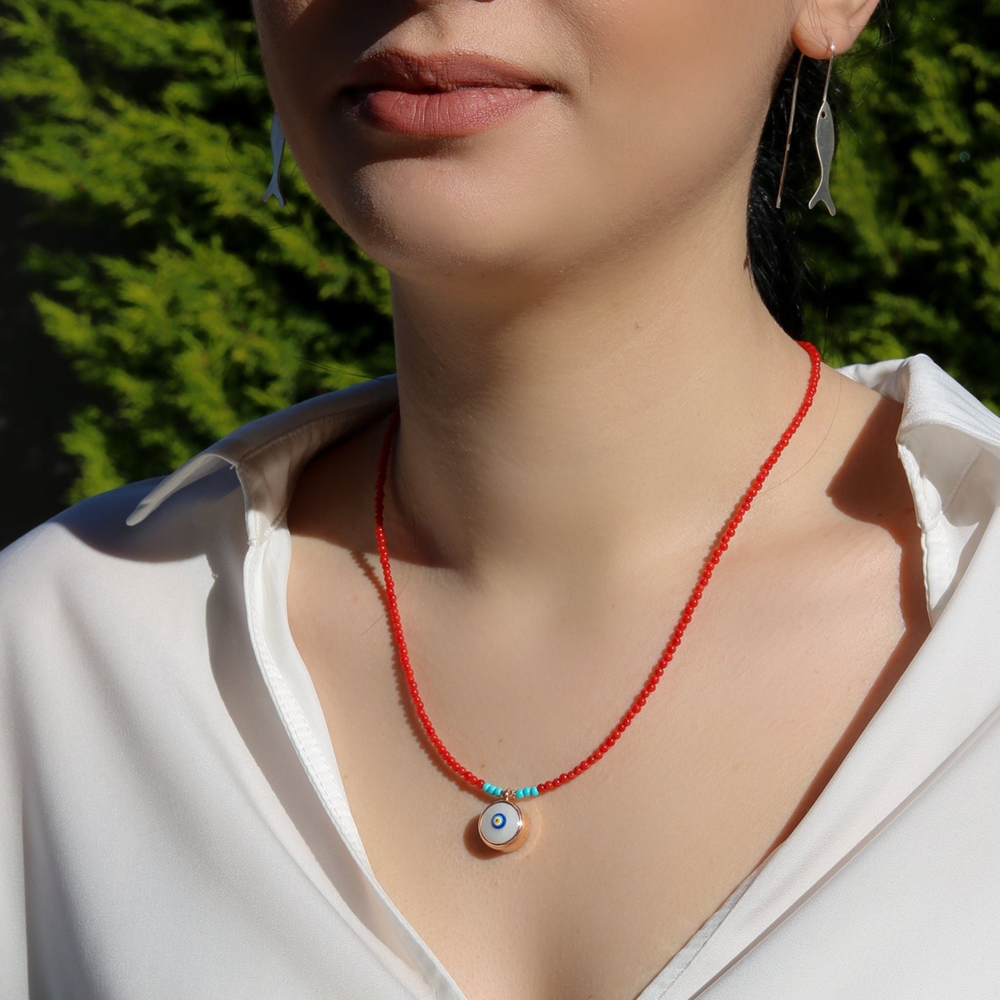 Woman wearing Evil Eye Coral Gemstone Necklace with red coral beads and evil eye pendant.