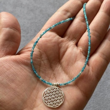 Hand holding a Flower of Life Apatite Necklace with blue beads and intricate silver pendant