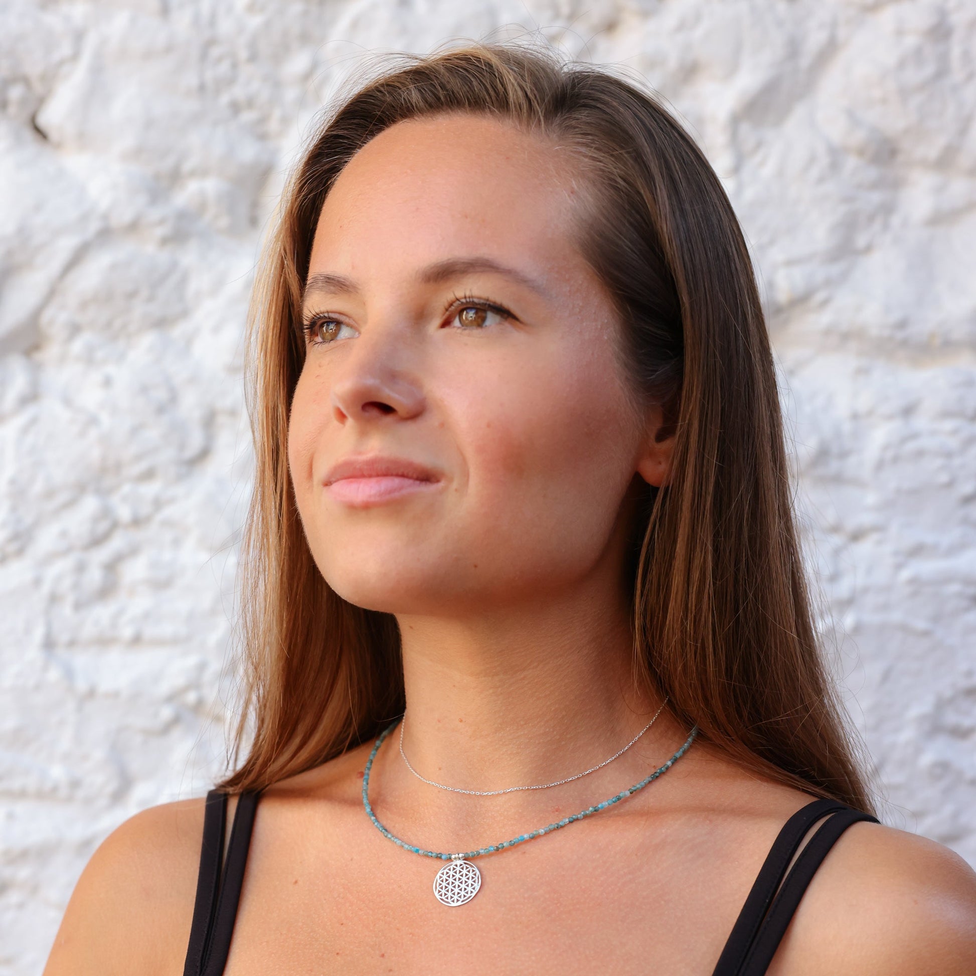 Woman wearing a Flower of Life Apatite Necklace against a textured white background.