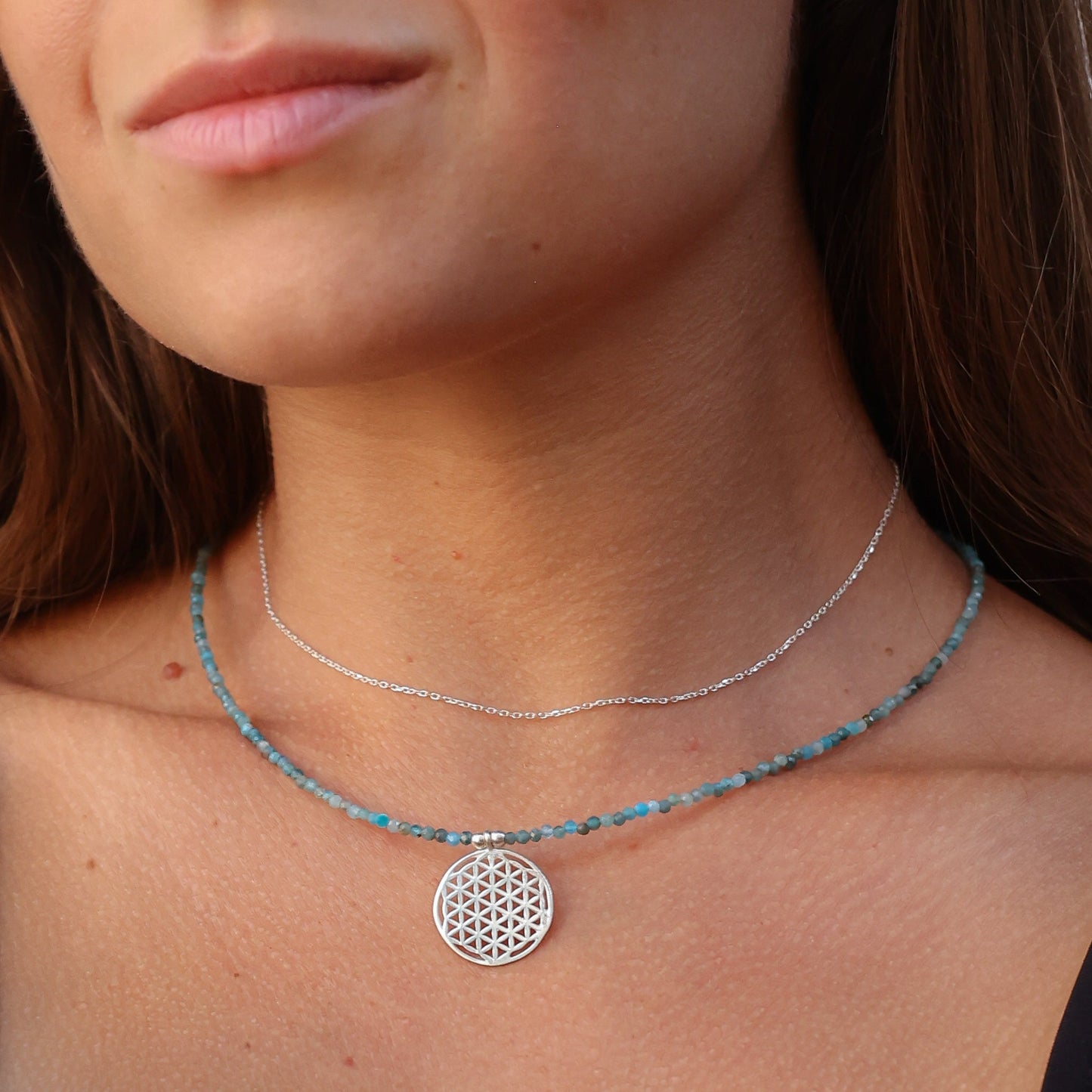 Close-up of Flower of Life Apatite Necklace worn by a woman, featuring blue beads and a silver geometric pendant.