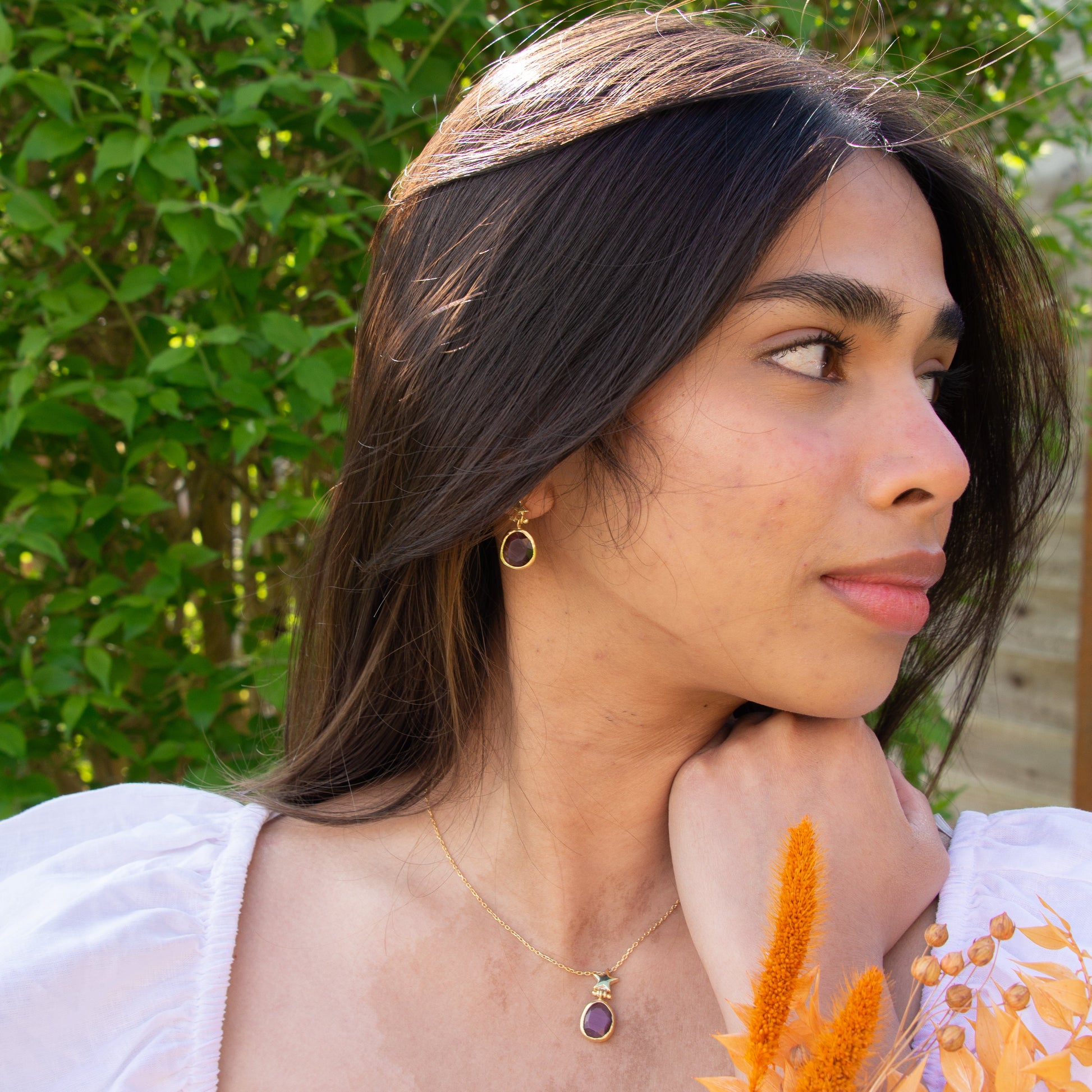 Woman wearing Foligno Purple Cat's Eye Stone Silver Chain Necklace and Earrings Set, standing amidst greenery.