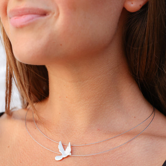 Close-up of woman wearing Free Bird on a Wire Silver Necklace, featuring a delicate silver bird pendant on thin wire chains.