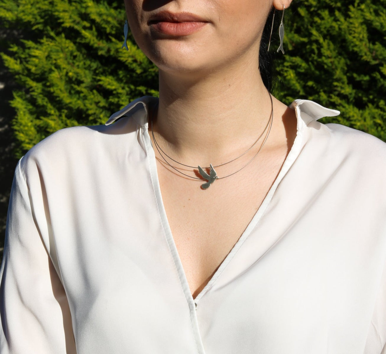 Woman wearing Free Bird on a Wire Silver Necklace and white blouse outdoors