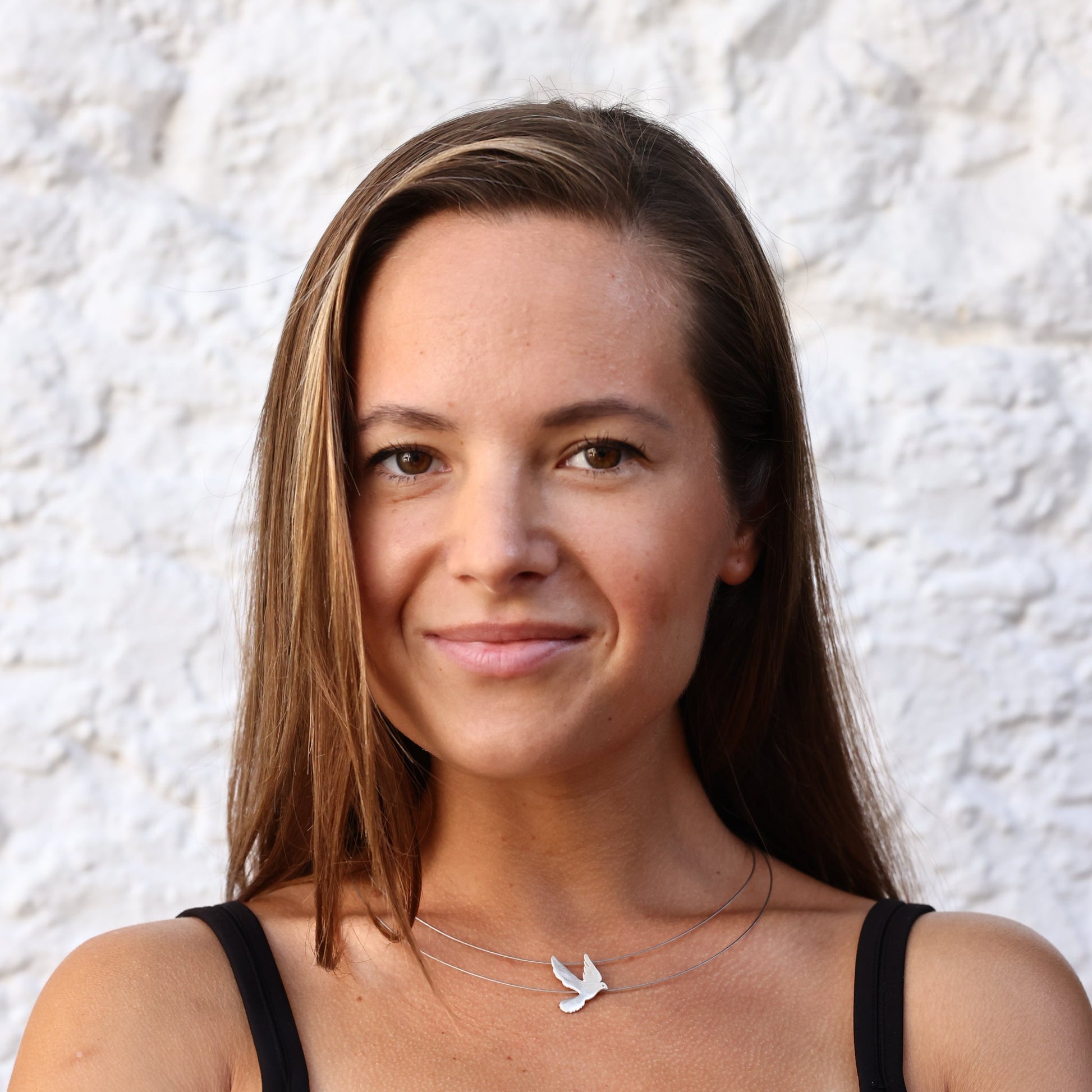 Woman wearing Free Bird on a Wire Silver Necklace against a white textured wall.