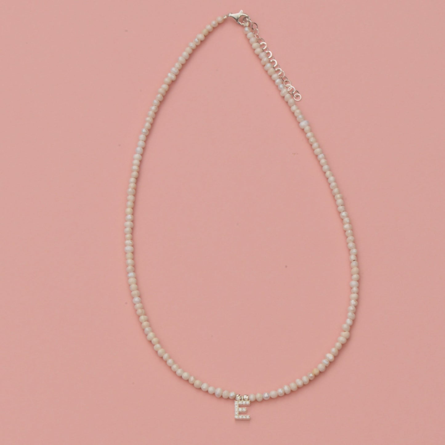 Freshwater Pearls Initial Necklace with gold 'E' pendant on a pink background