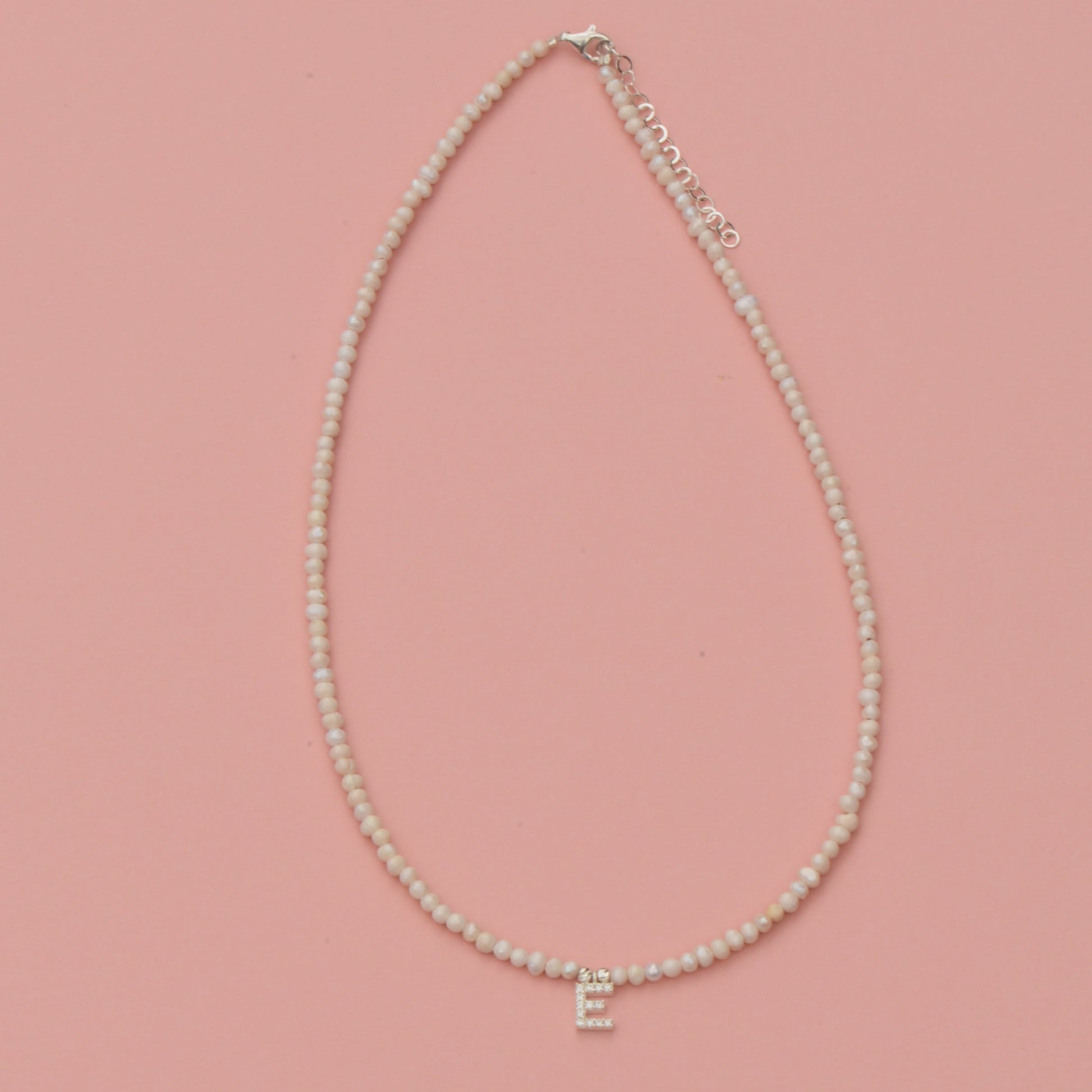 Freshwater Pearls Initial Necklace with gold 'E' pendant on a pink background