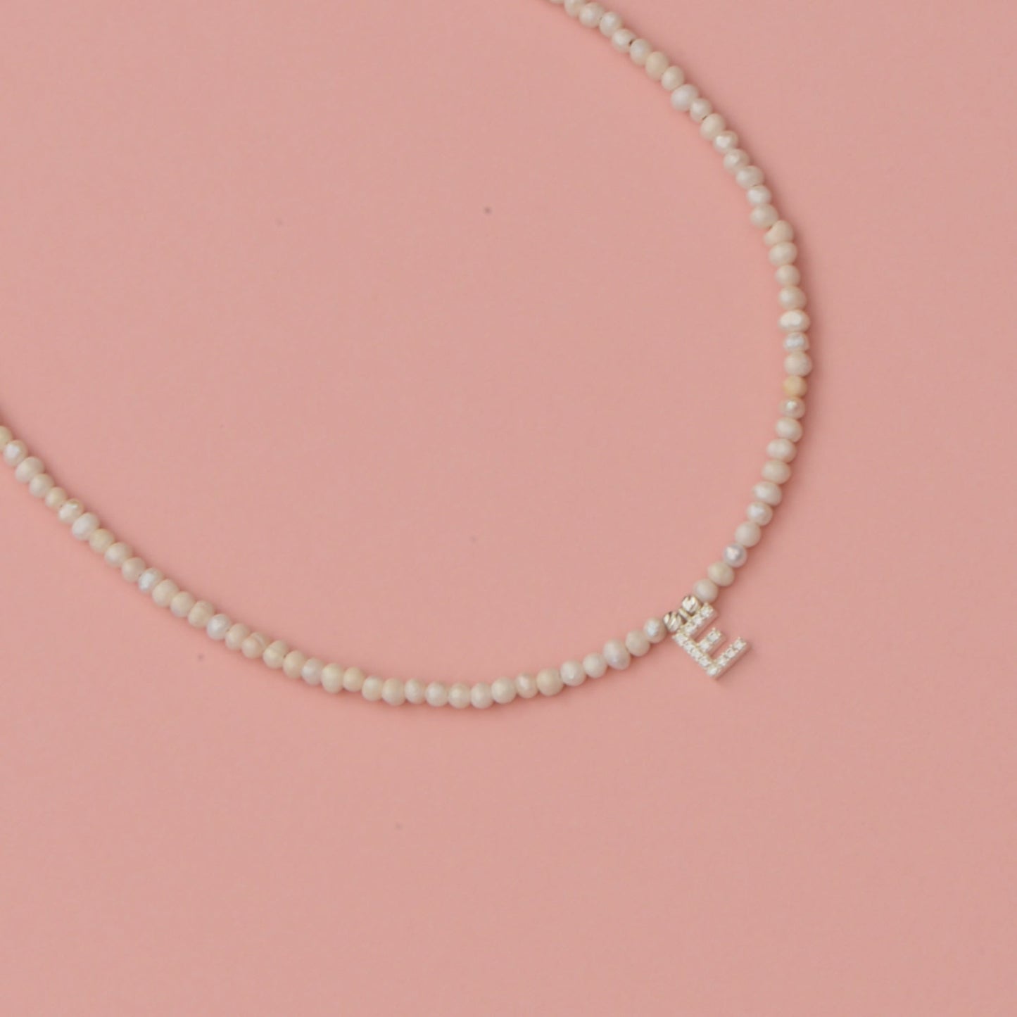 Freshwater Pearls Initial Necklace with a sparkling initial pendant on a pink background