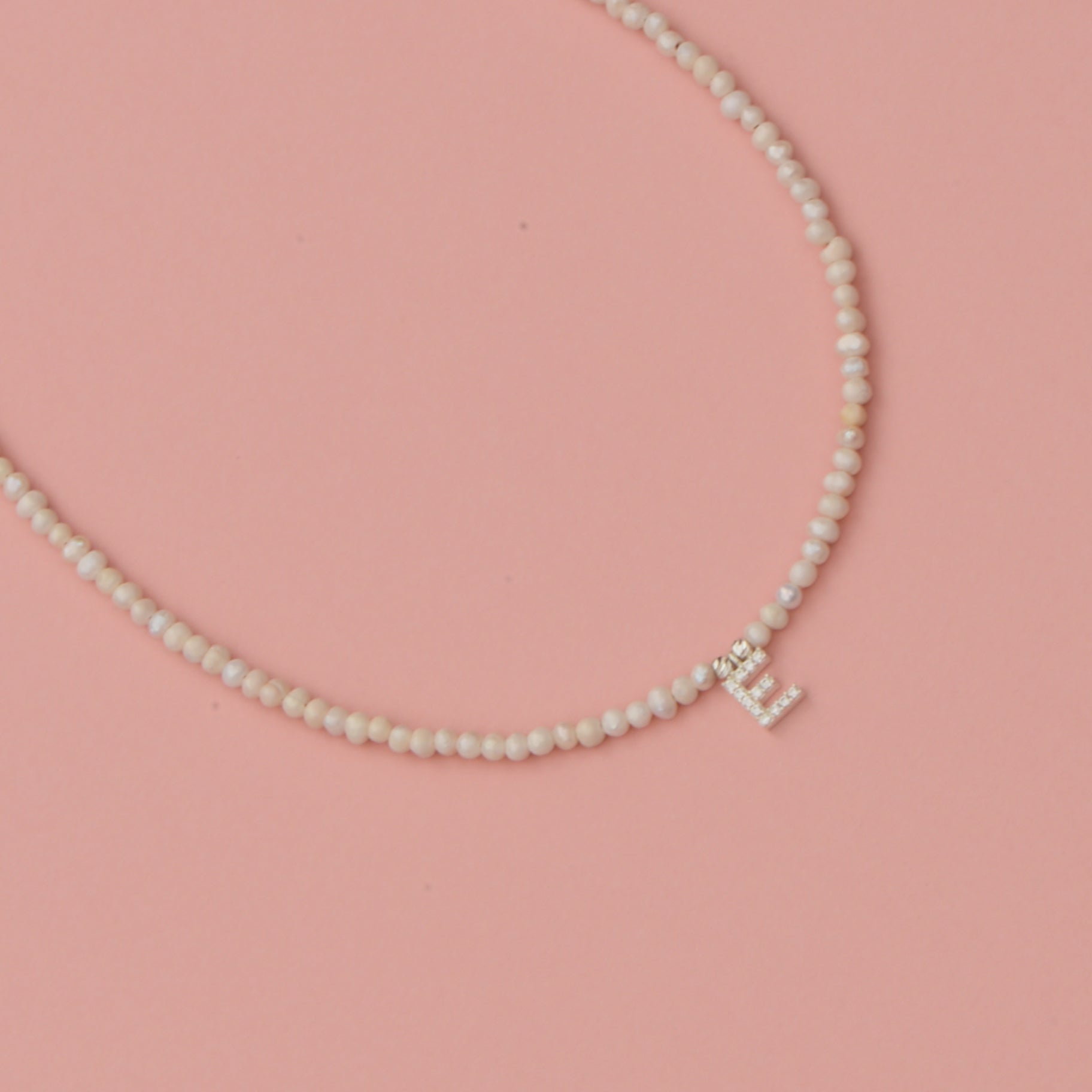 Freshwater Pearls Initial Necklace with a sparkling initial pendant on a pink background