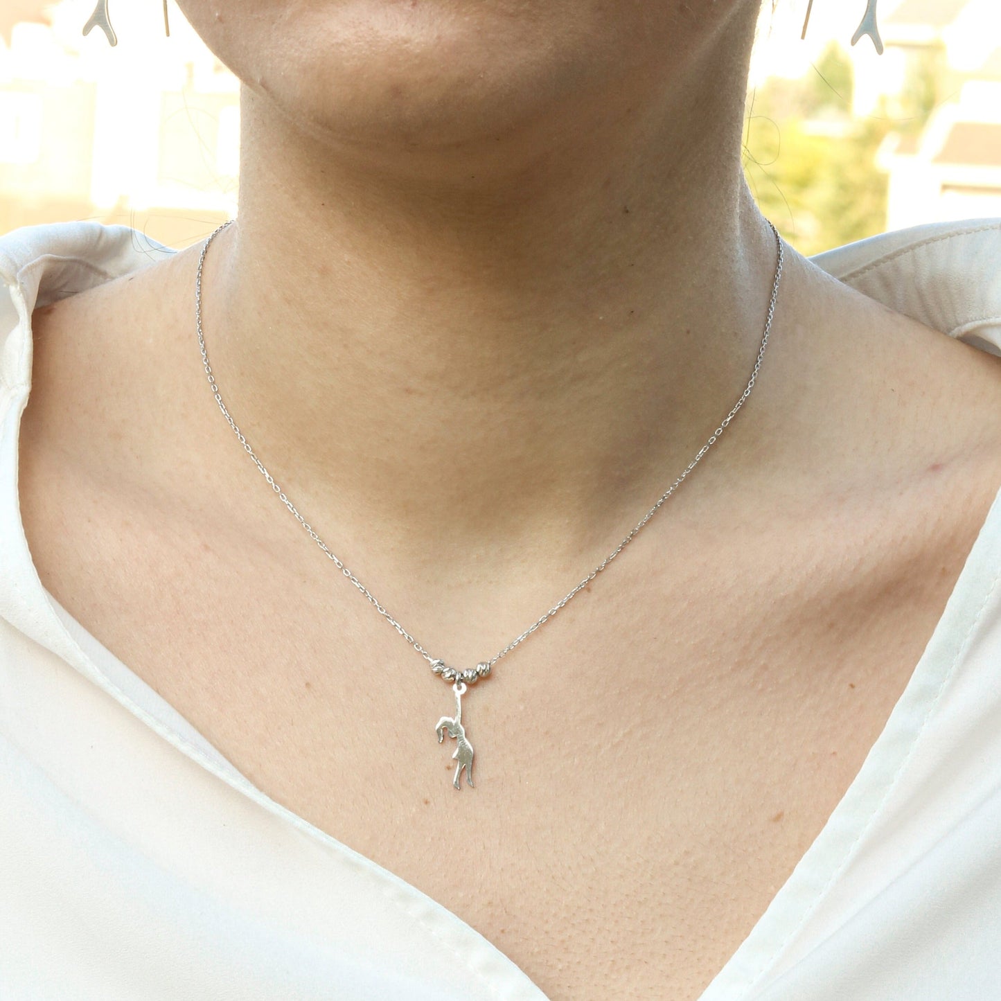 Close-up shot of a Girl With Balloons Silver Necklace worn by a person in a white blouse.