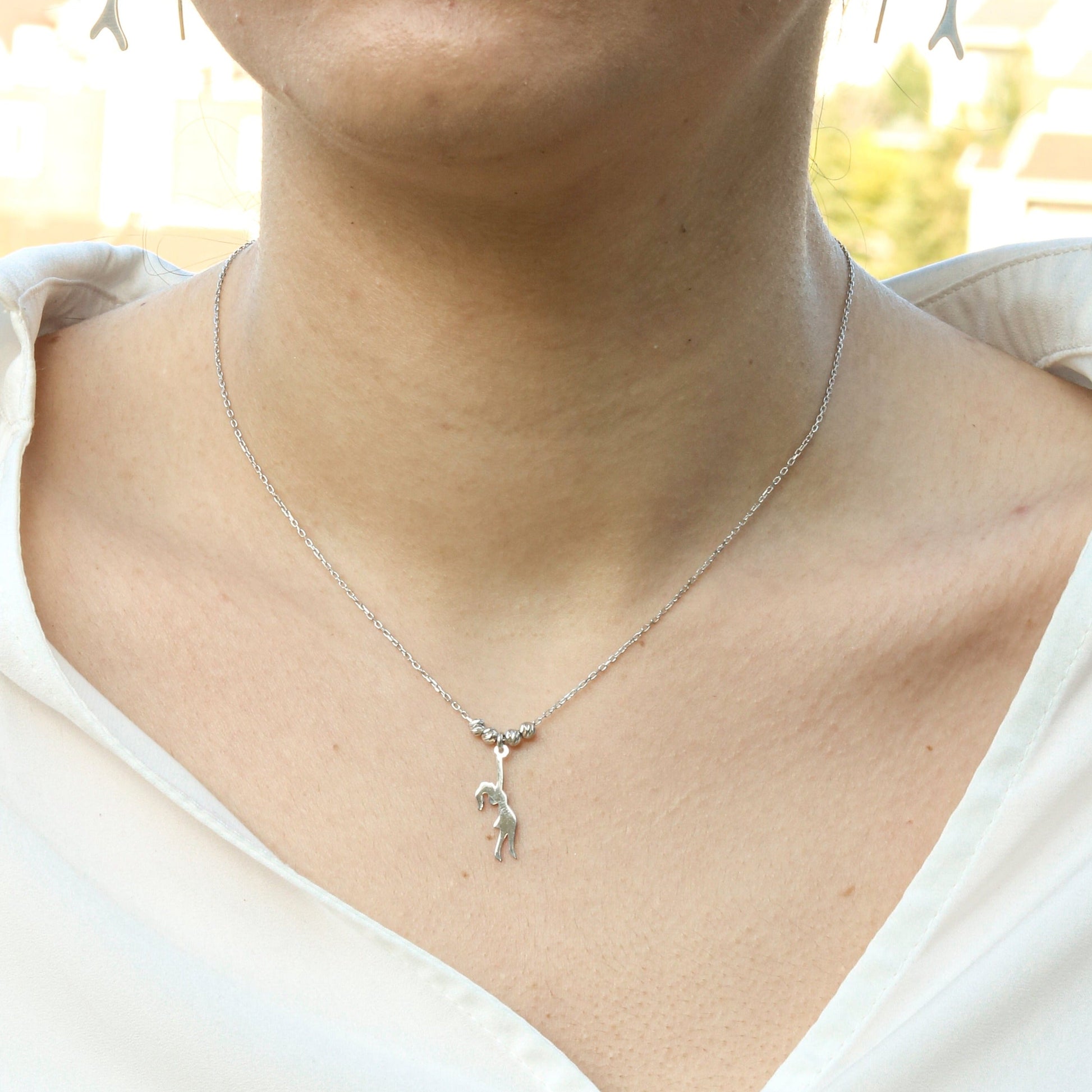 Close-up shot of a Girl With Balloons Silver Necklace worn by a person in a white blouse.