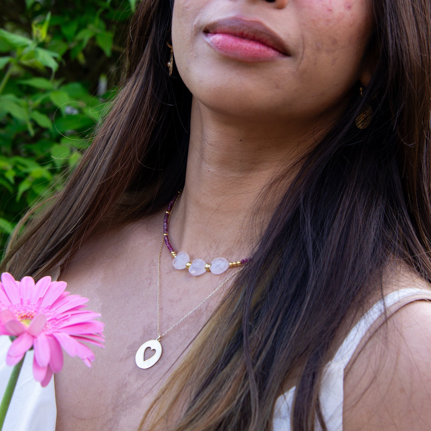 Woman wearing Heart in Silver Disc Necklace holding pink flower against green background.