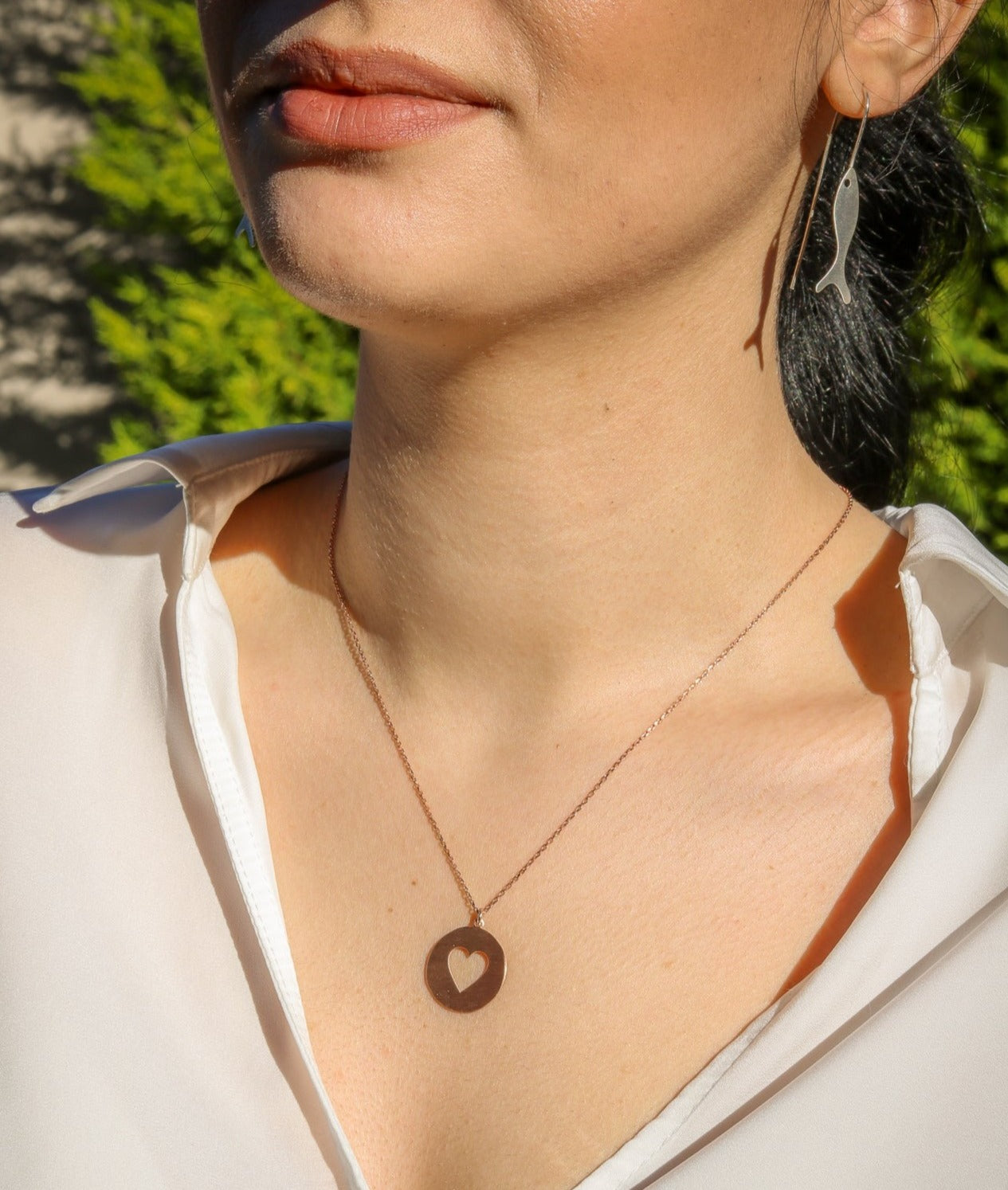 Woman wearing Heart in Silver Disc Necklace with white blouse, close-up shot.