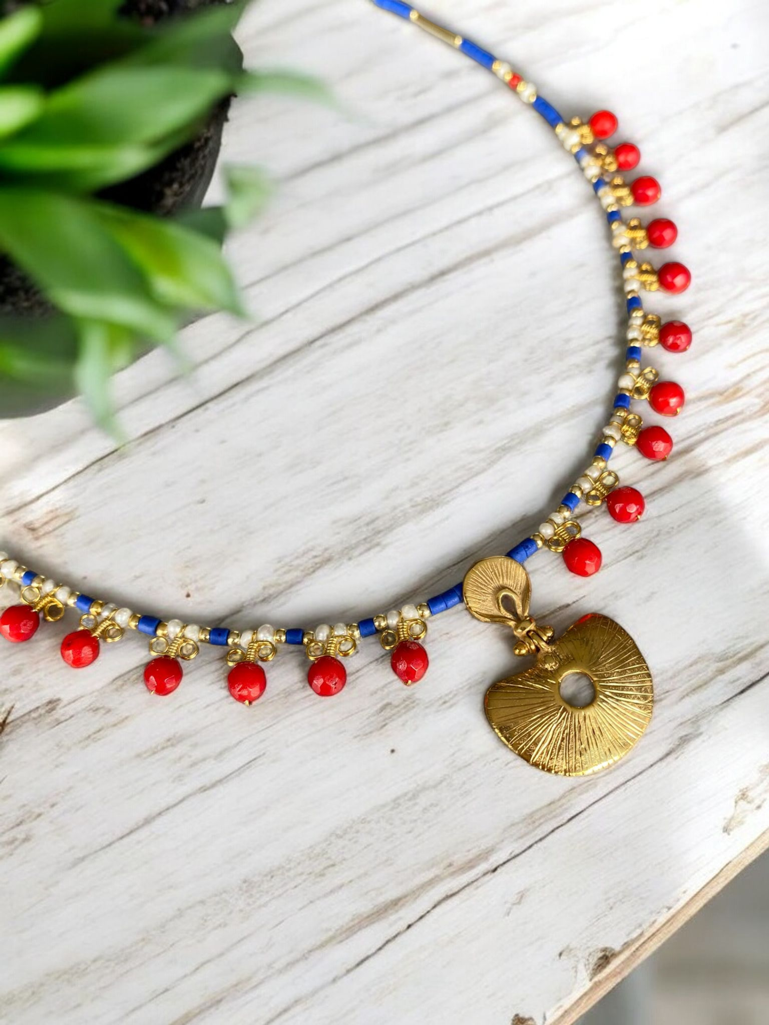 Hera Coral and Lapis Lazuli Gemstone Necklace in 925 Silver with Gold Plating on a white wooden surface, showcasing vibrant red and blue beads with a golden pendant.