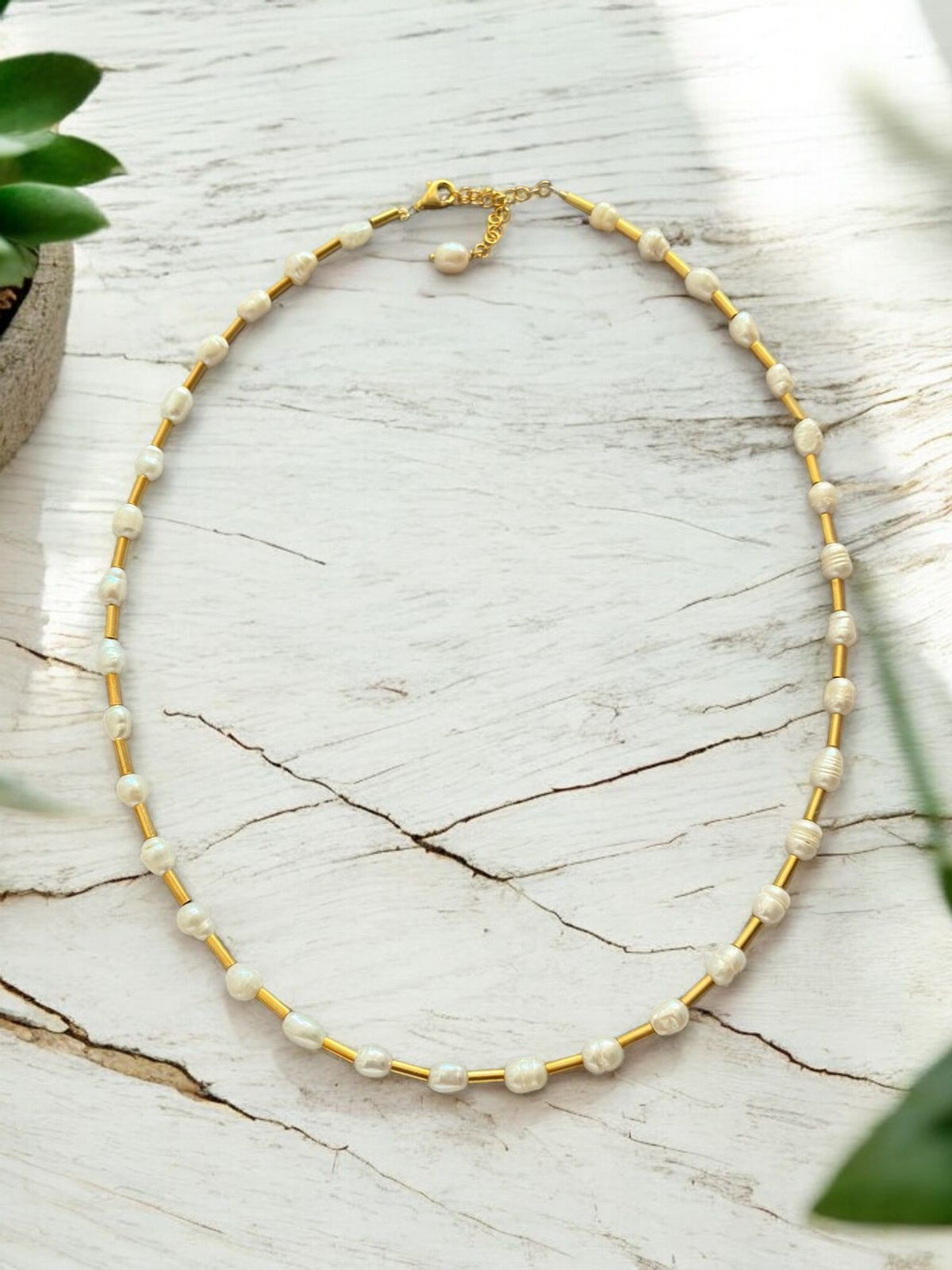 Jana Pearl and Silver Necklace - Gold Plated, displayed on a white wooden surface with greenery.