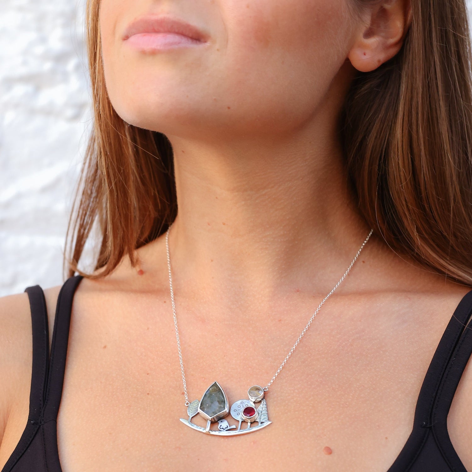 Close-up of a woman wearing a Landscape Silver Necklace with artistic tree and gemstone design