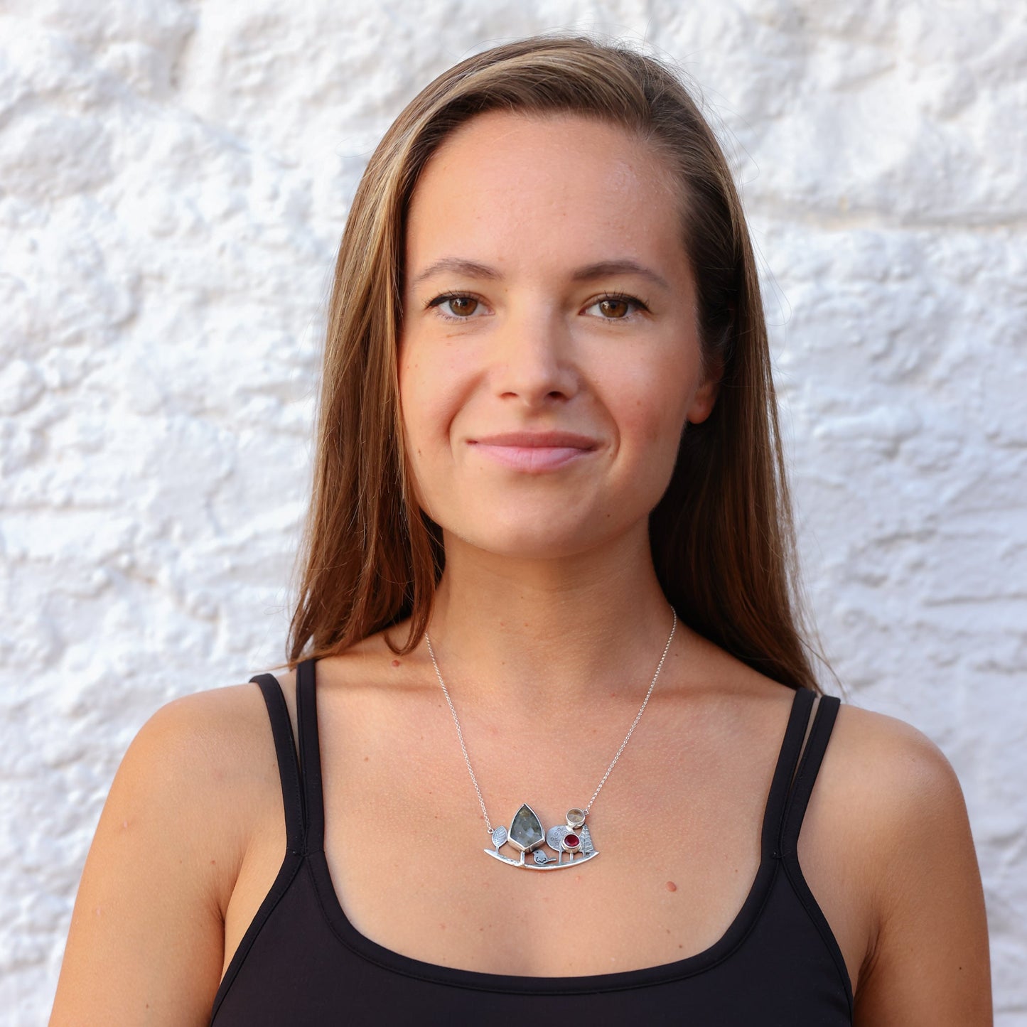 Woman wearing a Landscape Silver Necklace with gemstones, showcasing its elegant design on her neck.