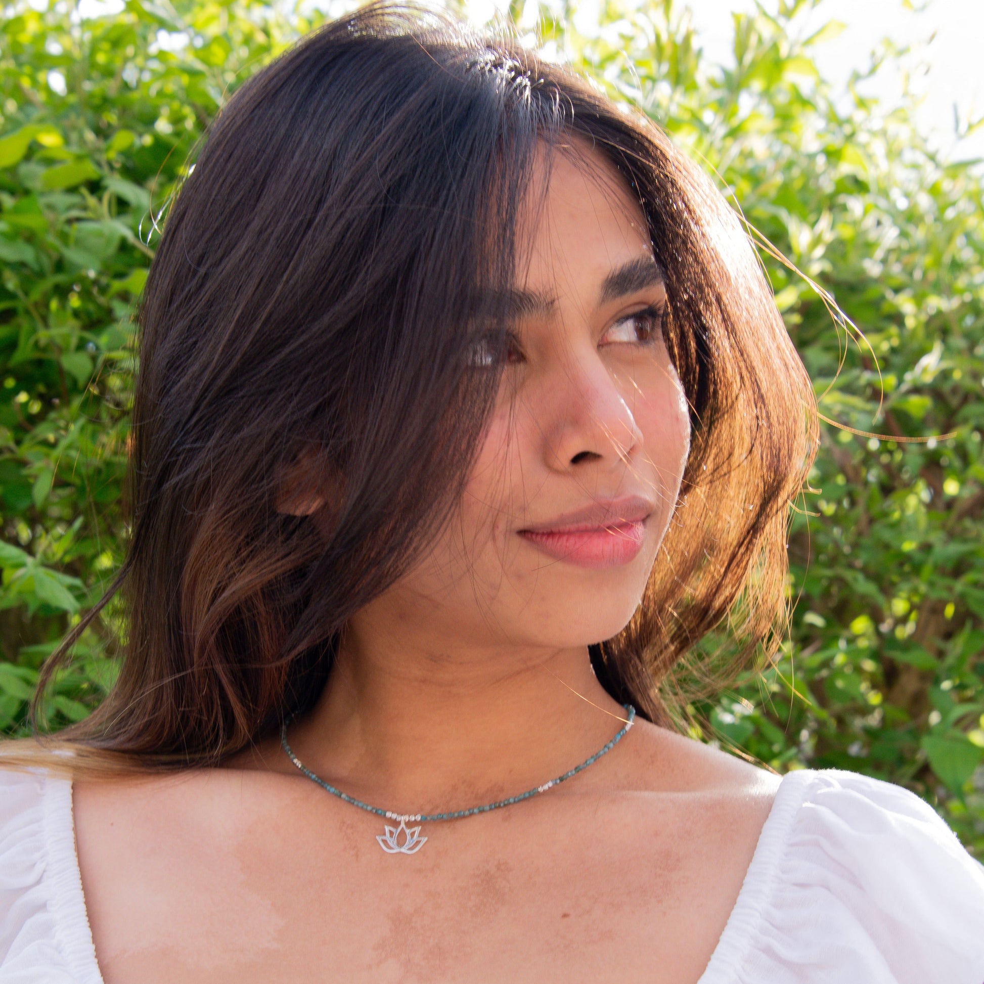 Woman wearing Lotus Flower Apatite Necklace against a backdrop of green foliage.