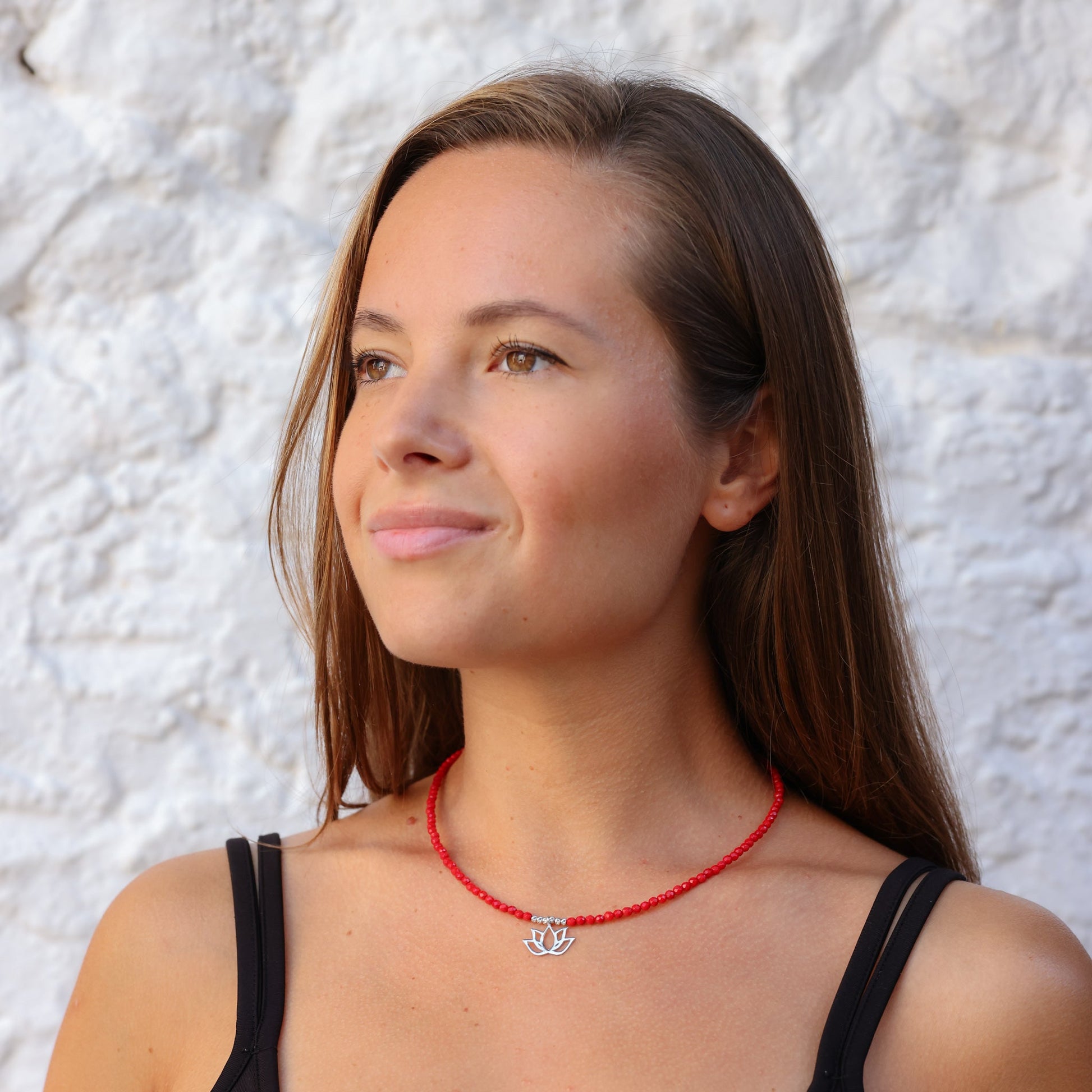 Woman wearing Lotus Flower Coral Gemstone Beaded Necklace featuring red coral beads and a silver lotus pendant.