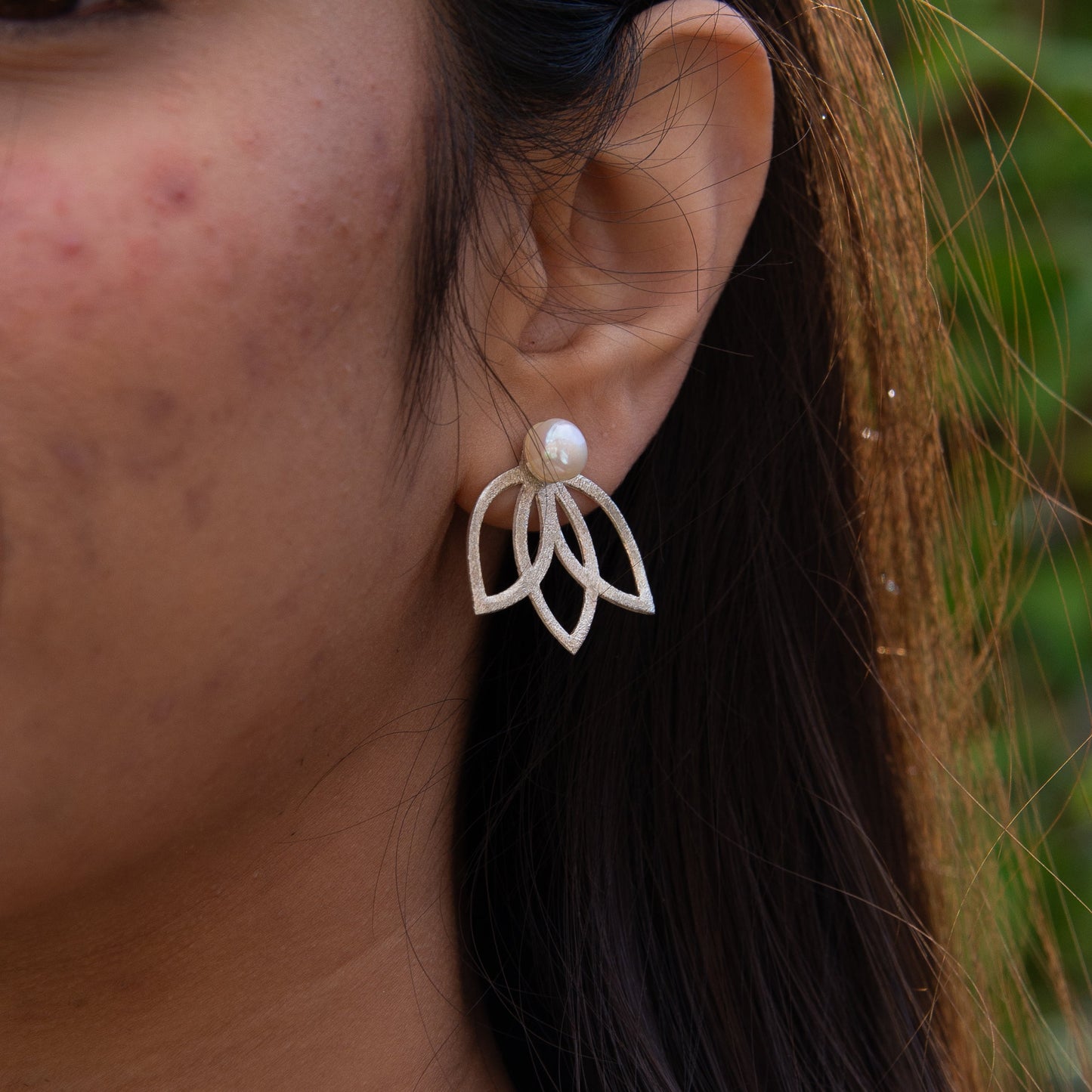 Close-up of a woman's ear wearing a Lotus Flower Silver and Freshwater Pearl Earring from a matching necklace and earring set.