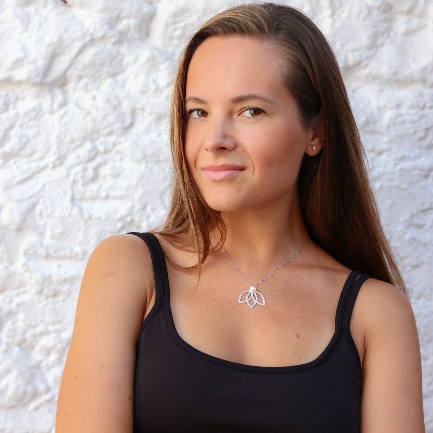 Woman wearing a silver and pearl lotus flower necklace, set against a white textured background