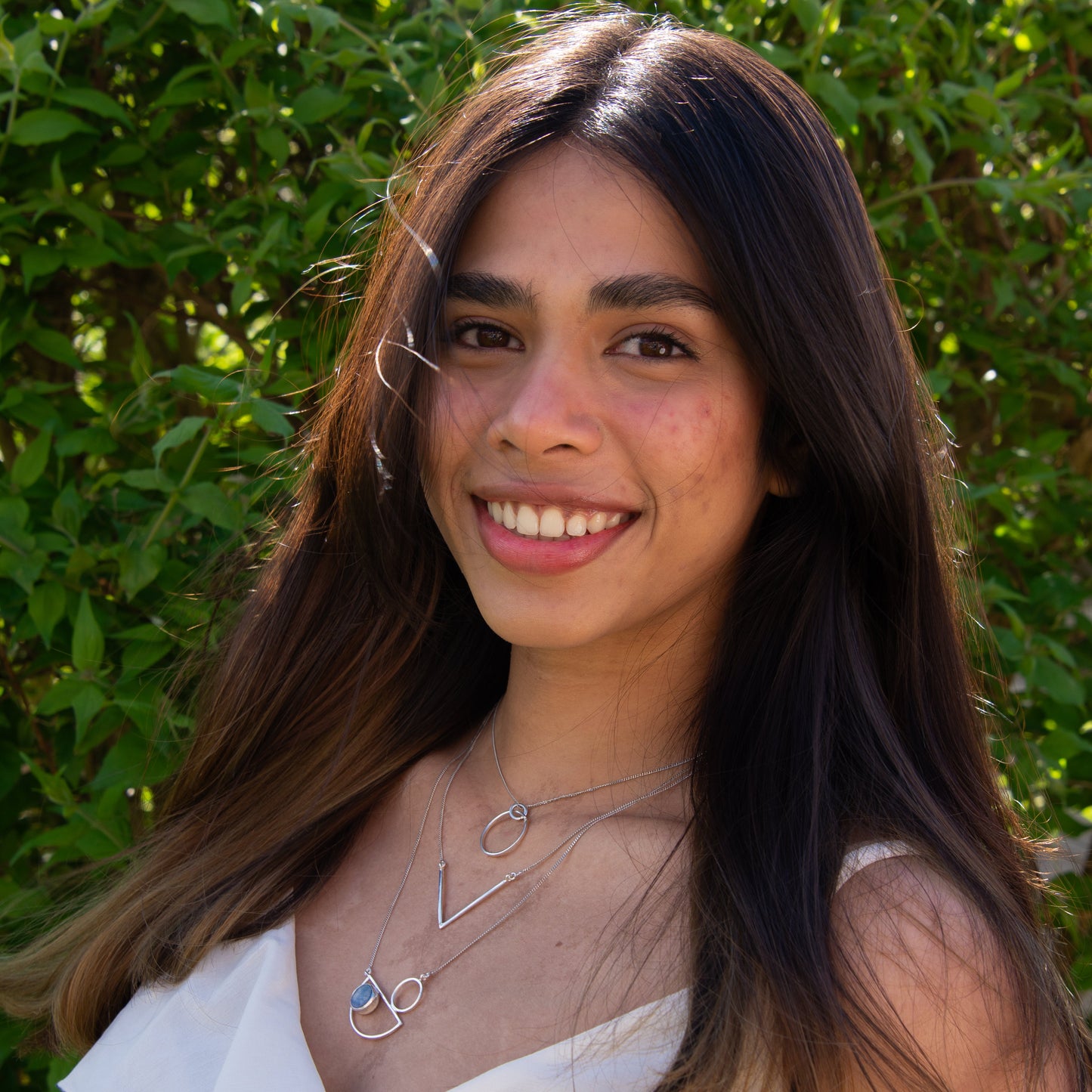 Smiling woman wearing Messina Layered Silver Necklace Set with greenery in the background.