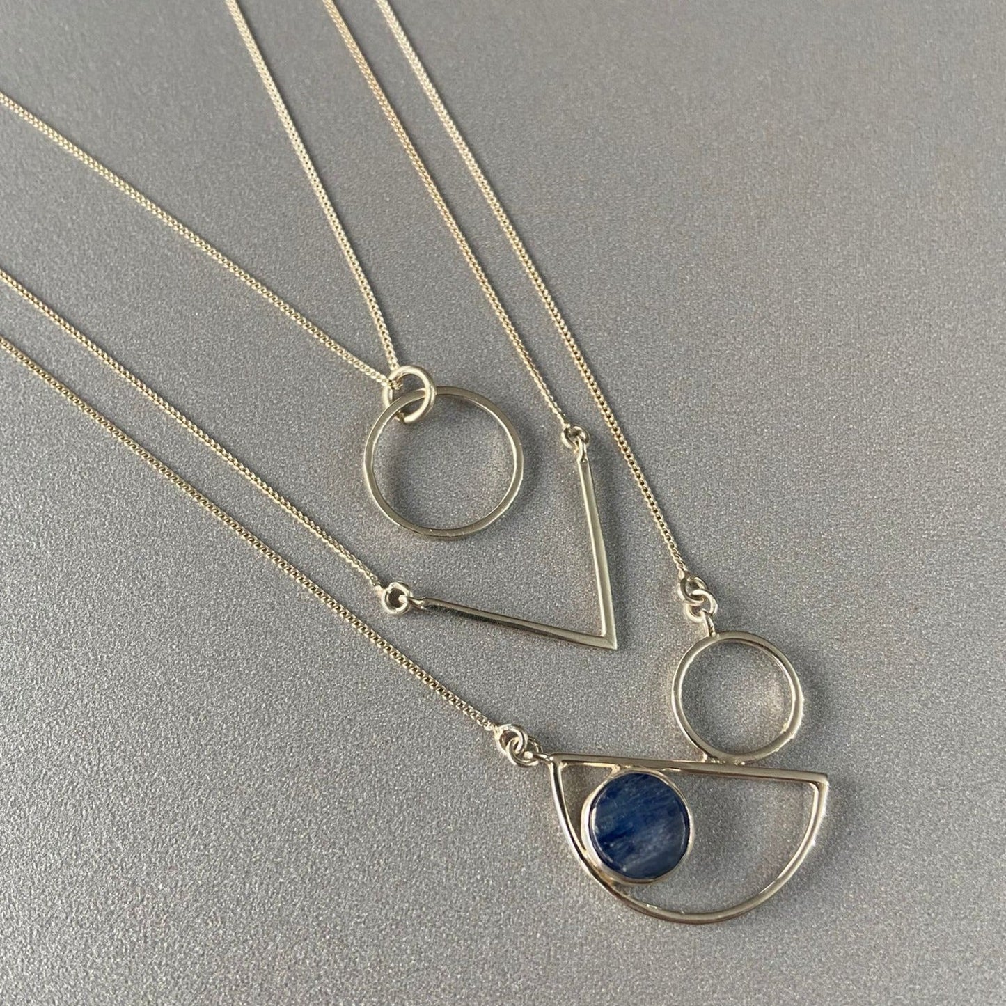 Messina Layered Silver Necklace Set with geometric shapes and blue stone on a grey background