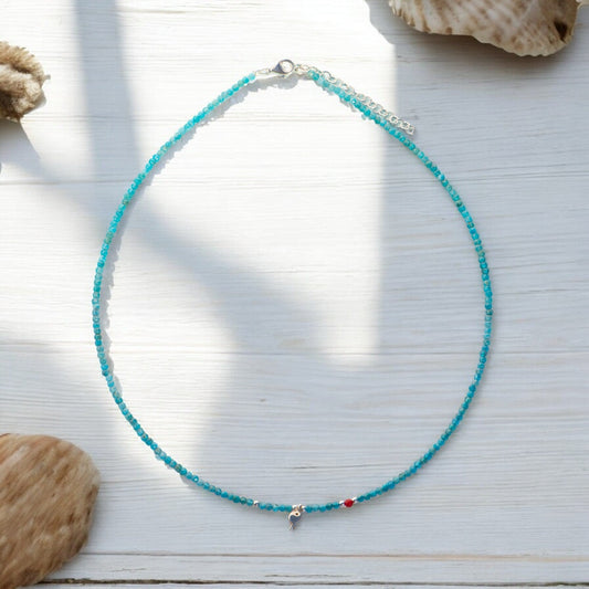 Minimal Apatite Gemstone Fish Necklace against a white wooden background with seashell accents.