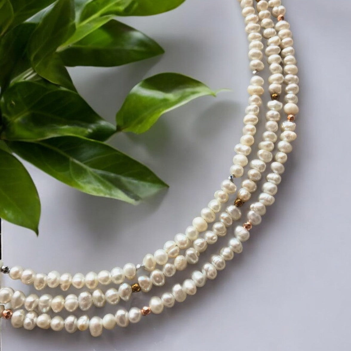 Multi Strand Pearl Necklace with Hematite and 925 Silver on a white background with leafy green plants in the corner.