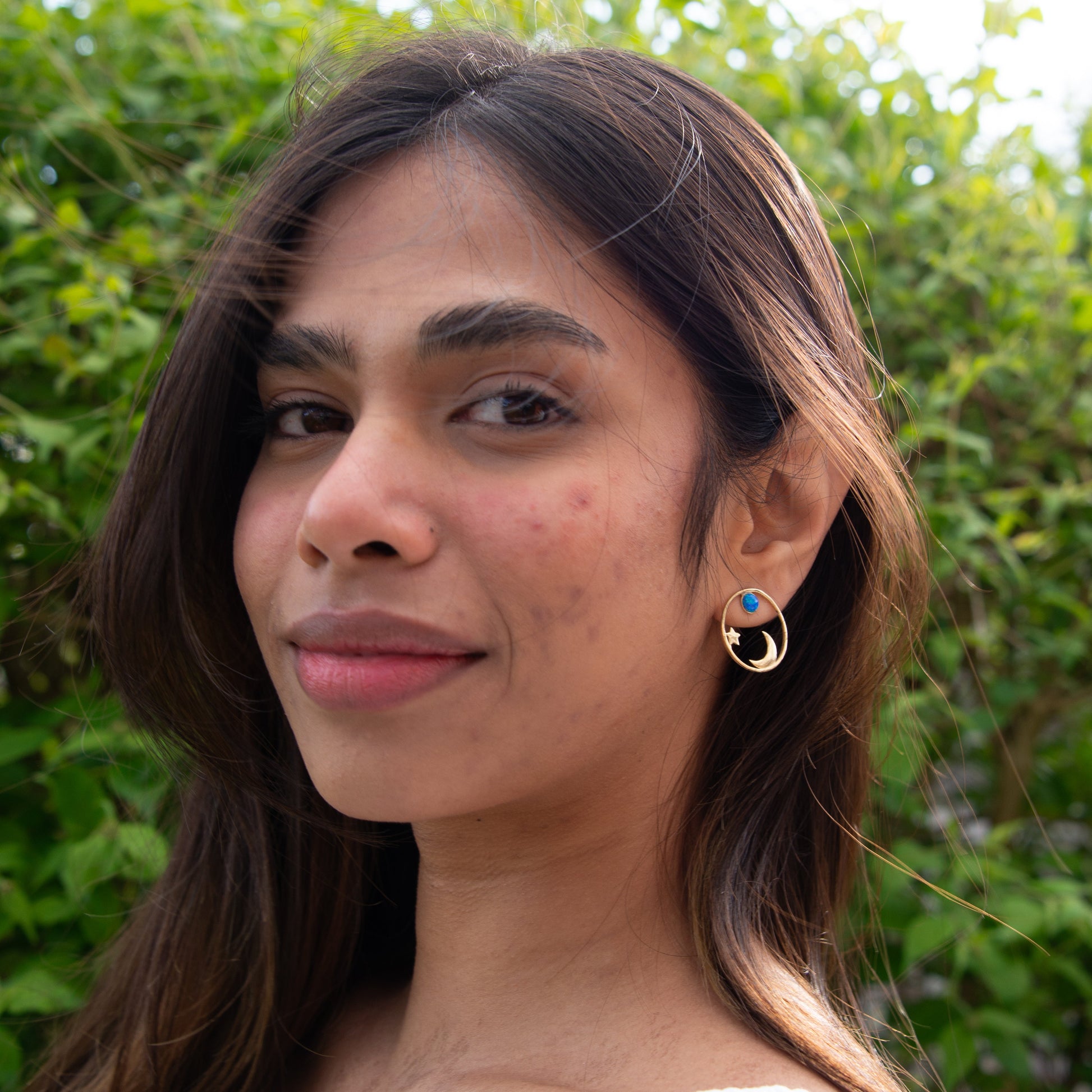 Model wearing My World Silver Earrings with blue accents against a green leafy background.