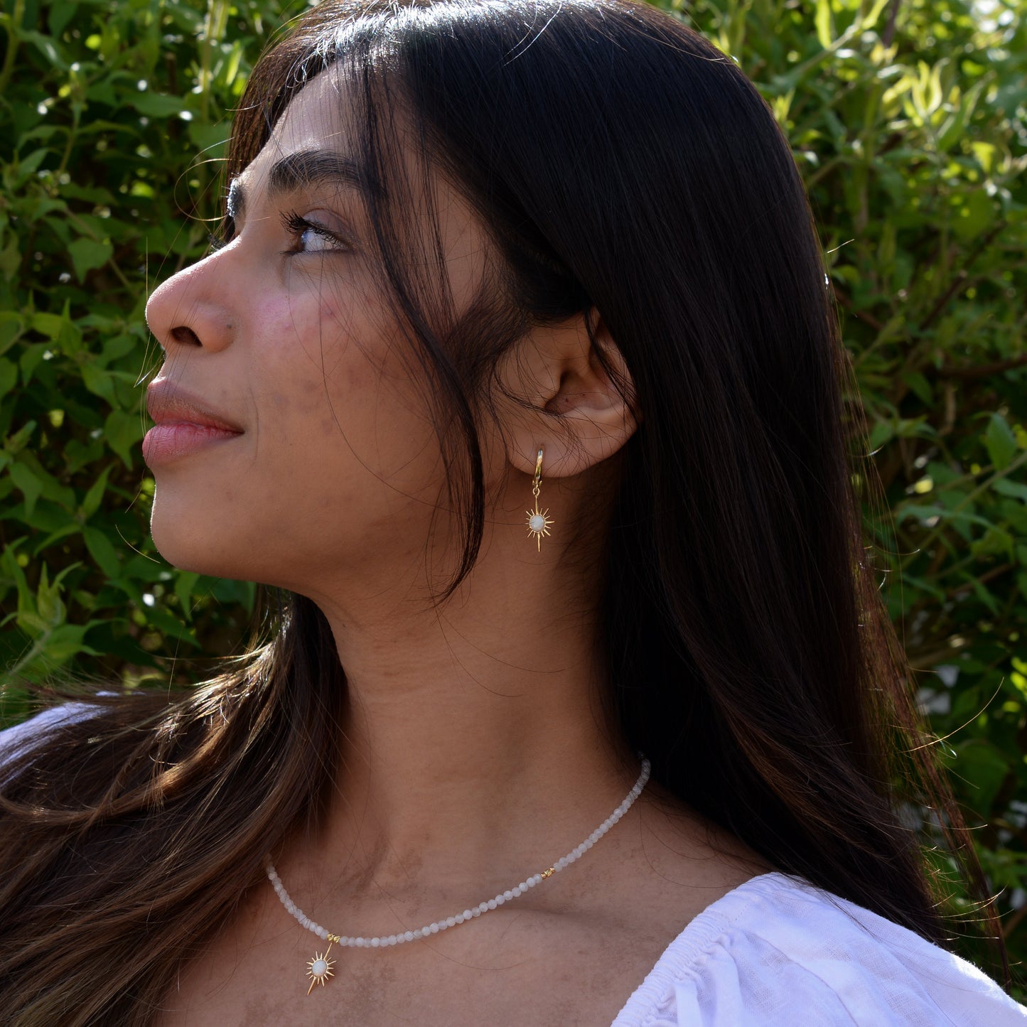 North Star Moonstone Dangle Drop Earrings worn by a woman with long hair, paired with a matching moonstone necklace in outdoor setting.