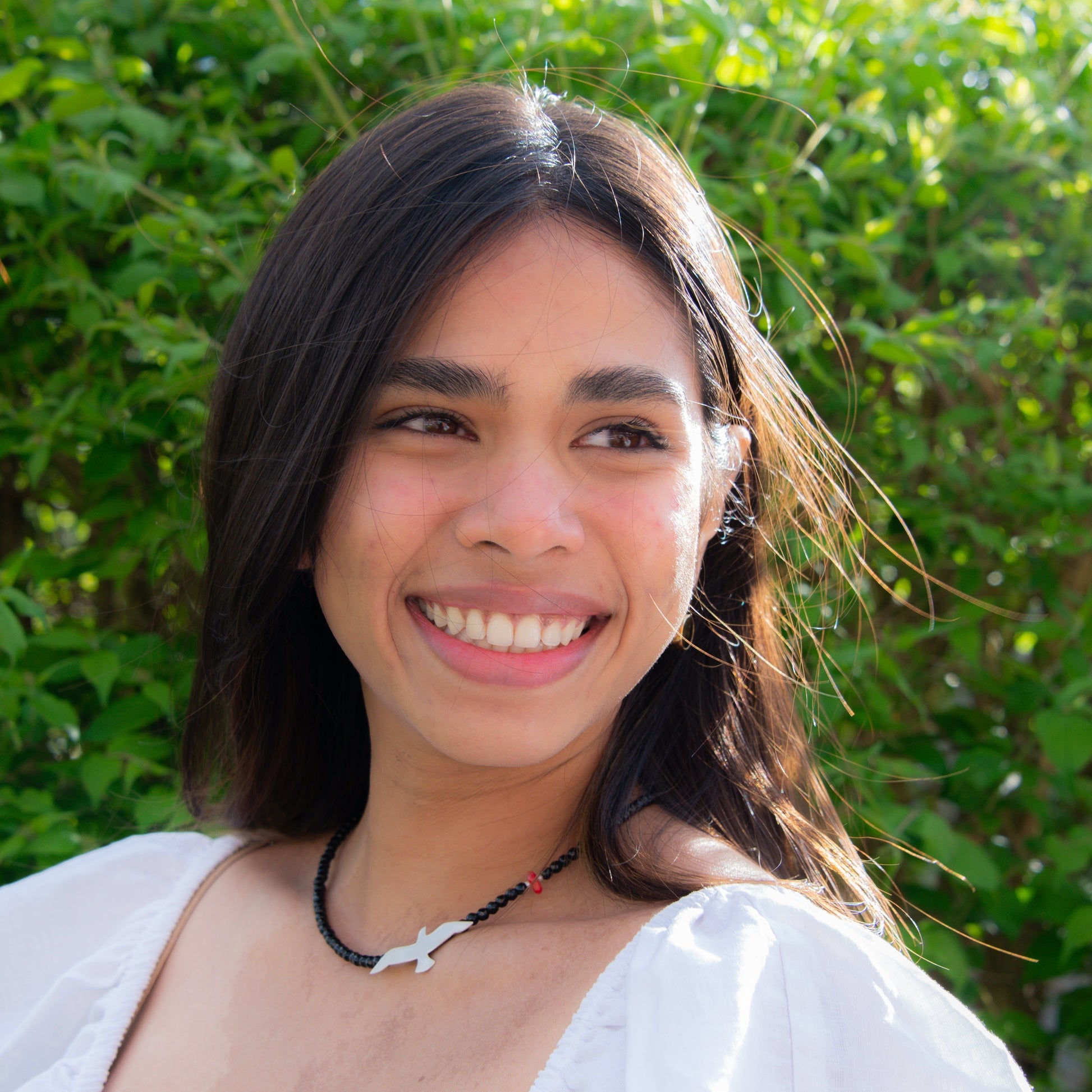 Smiling woman wearing Onyx Seagull and Red Bead Silver Necklace with green foliage background