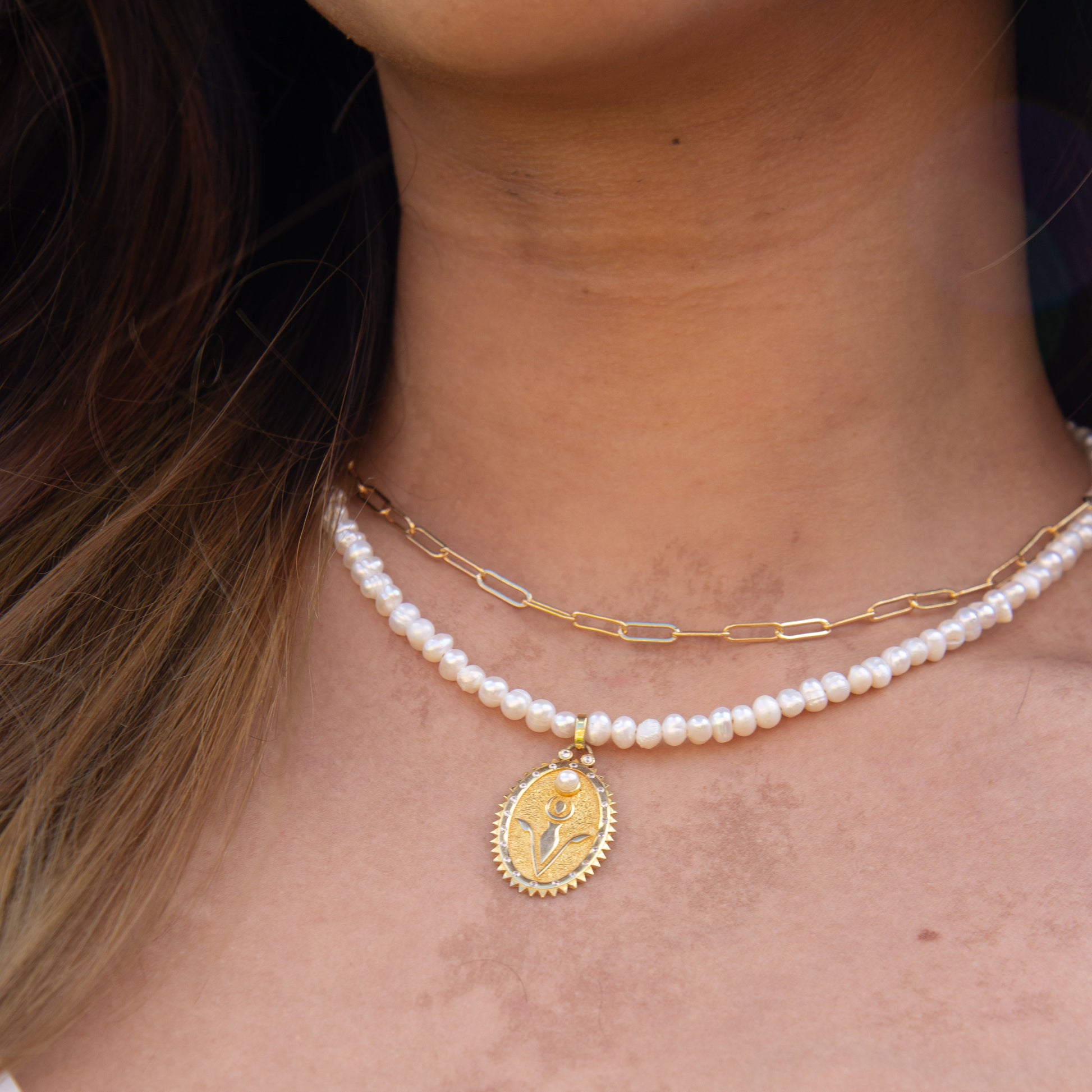 Close-up of Pearl Necklace featuring a gold Rebirth Symbol Plate Pendant worn on a woman's neck.