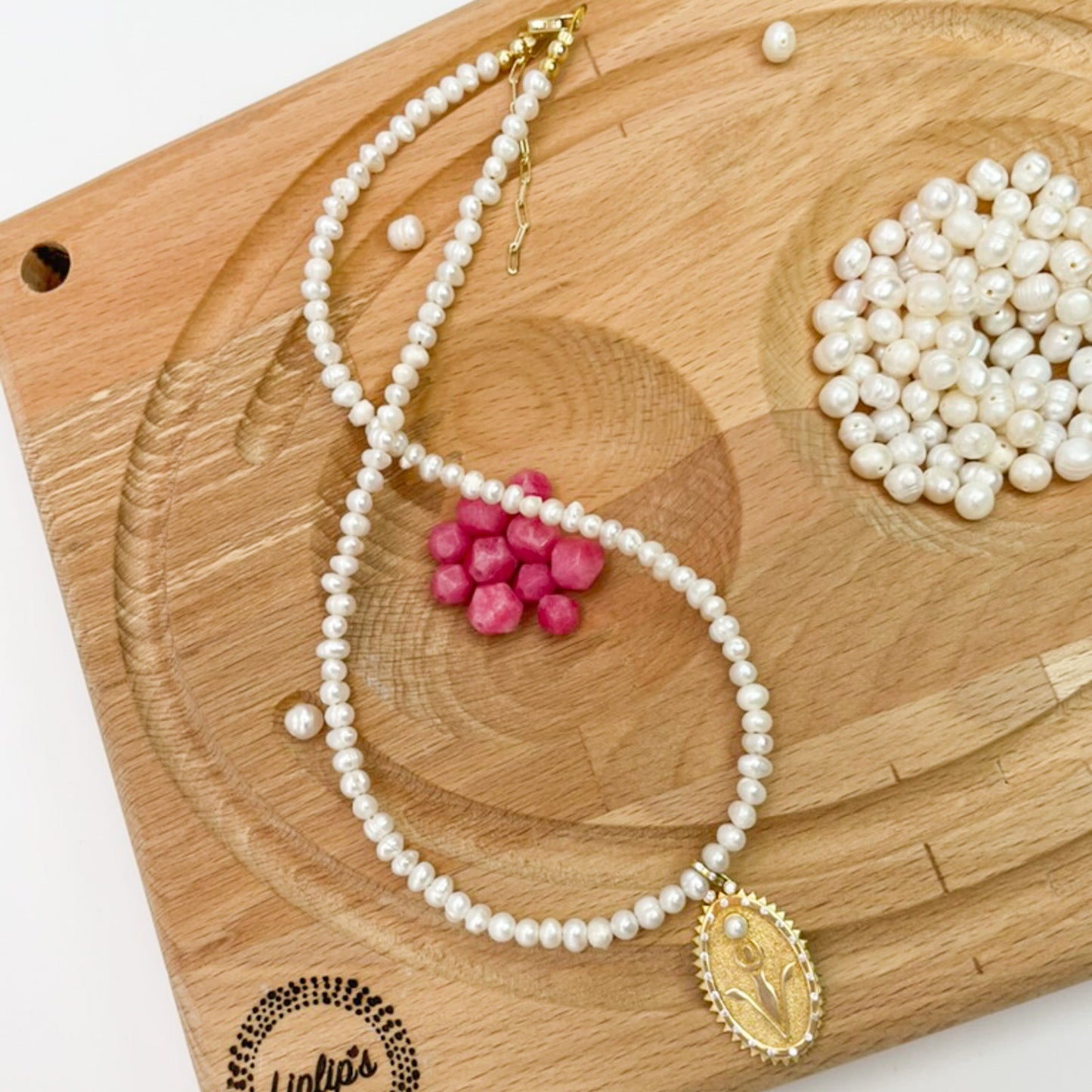 Pearl Necklace with Rebirth Symbol Plate Pendant showcased on a wooden board.