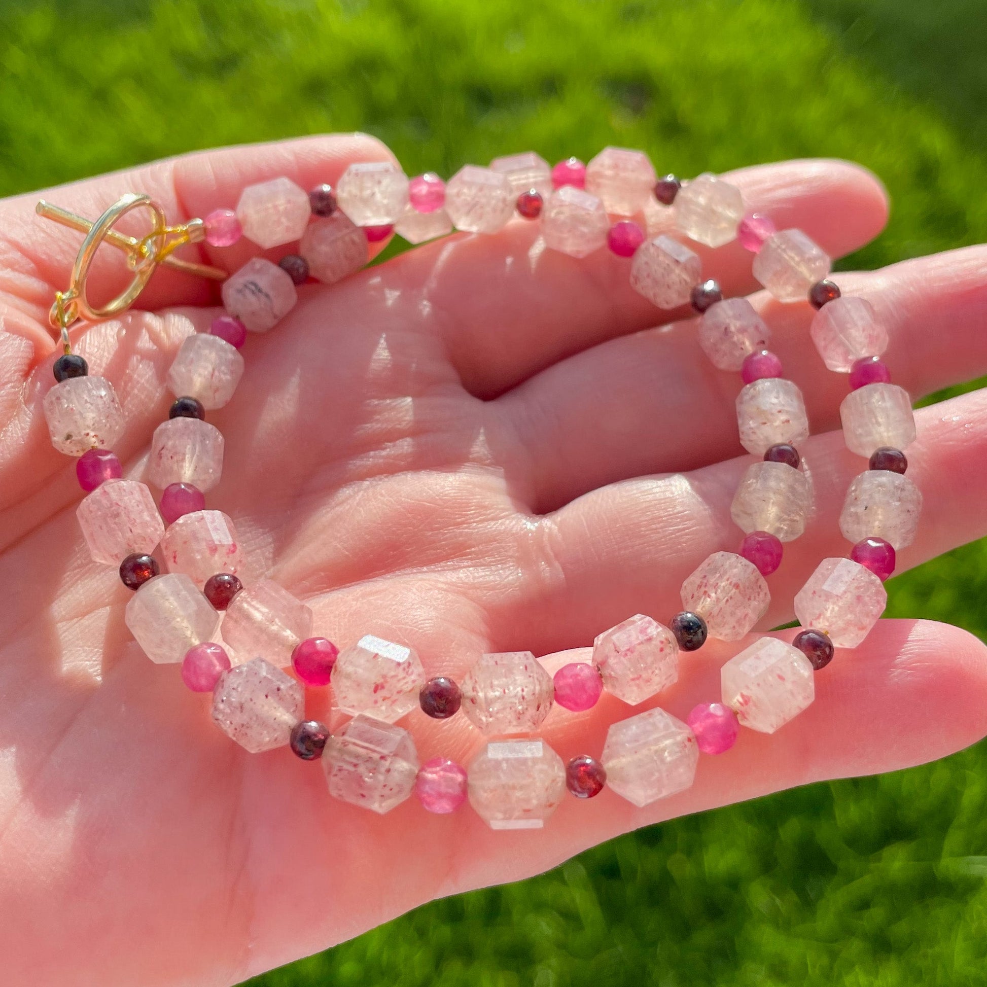 Hand holding a Pinky Strawberry Quartz Gemstone Necklace with bright sunlight reflecting on faceted beads.