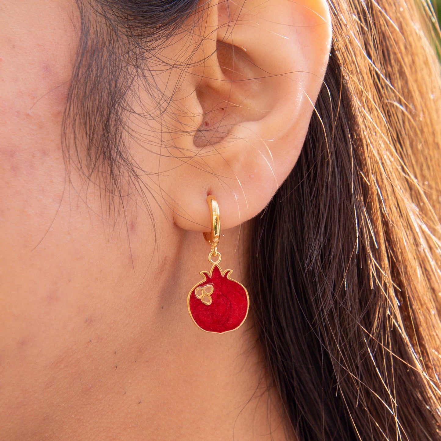 Close-up of Pomegranate Gold Plated Silver Dangle Hoop Earrings worn on a person’s ear.