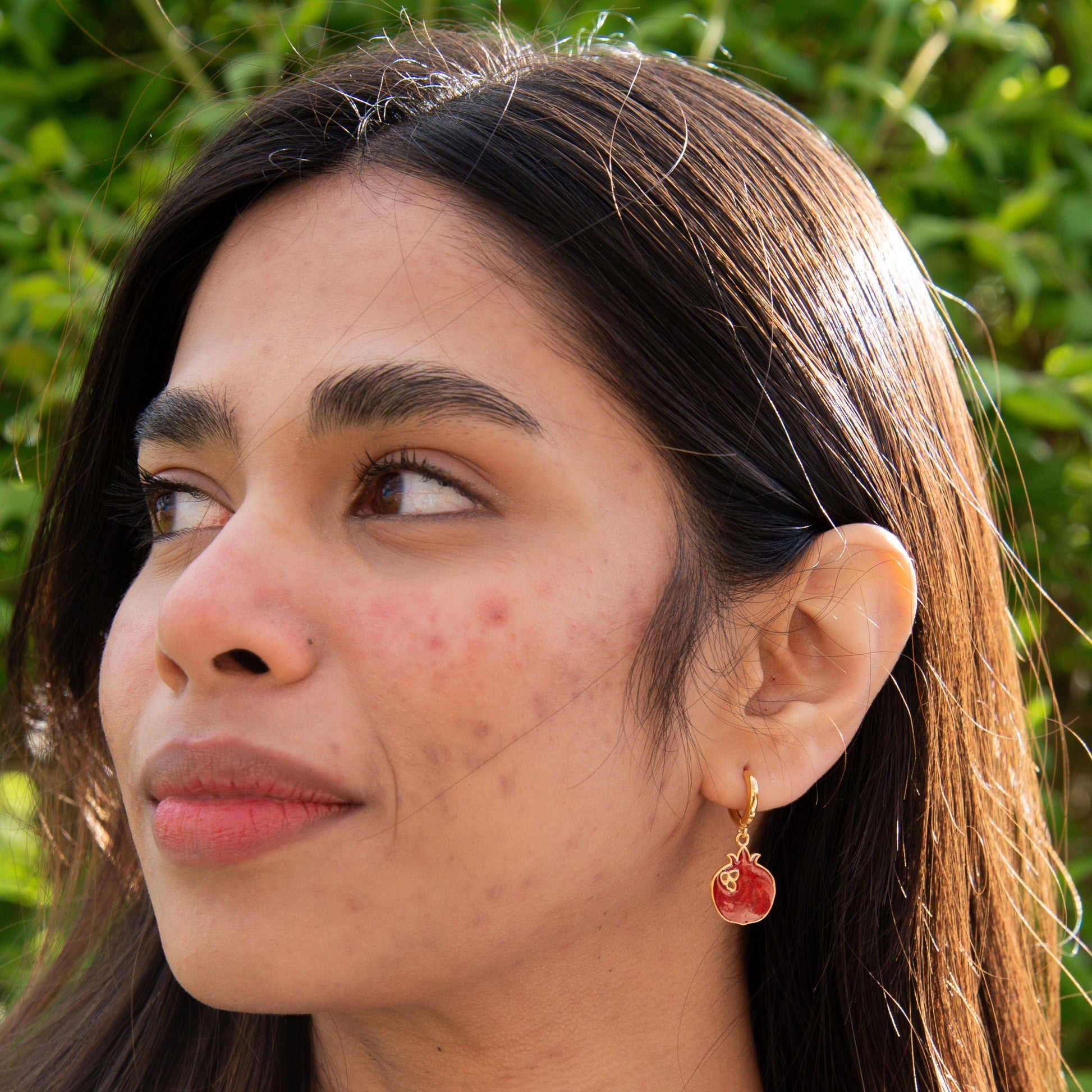 Close-up of woman wearing Pomegranate Gold Plated Silver Dangle Hoop Earrings against a green background.