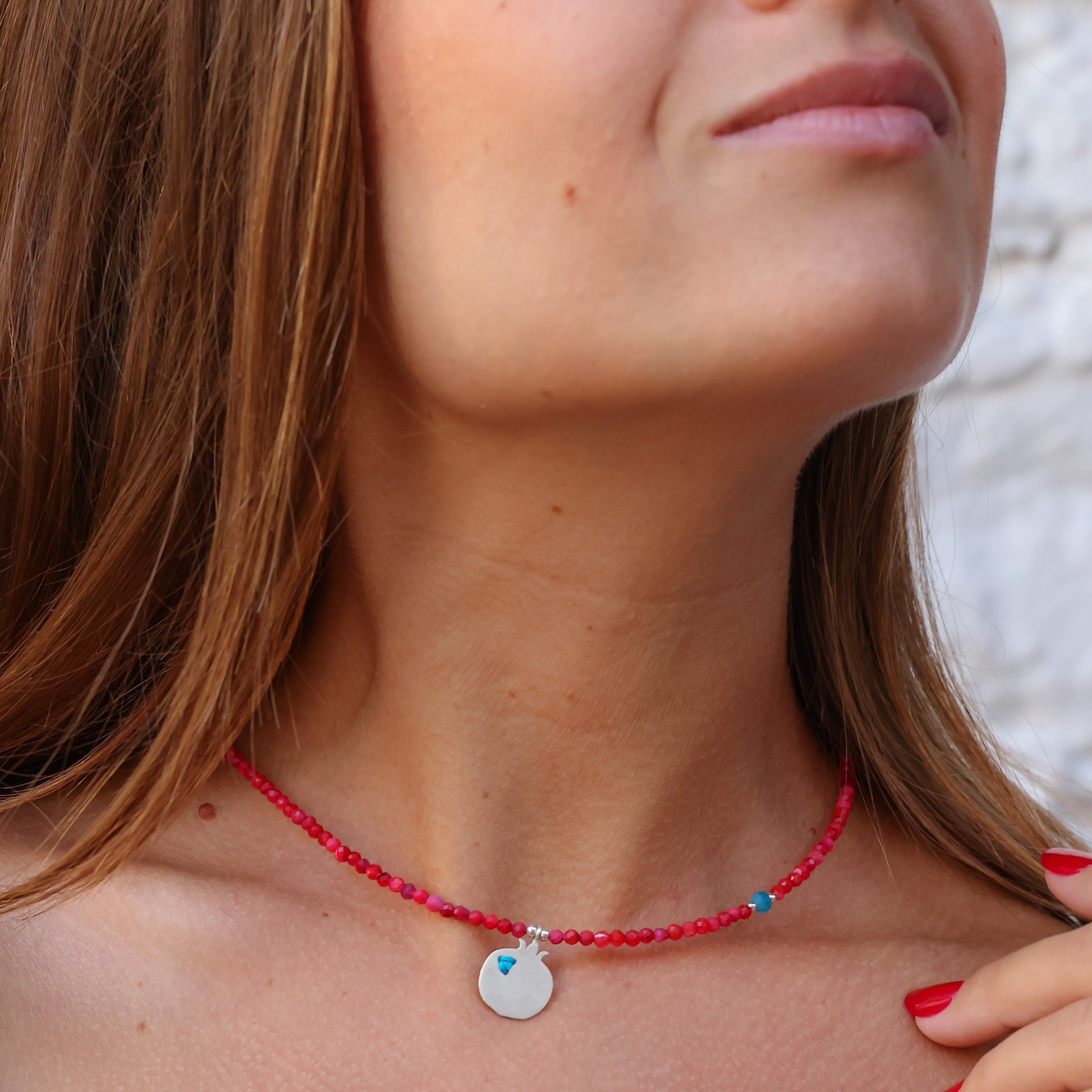 Close-up of woman wearing a Pomegranate Silver and Coral Necklace with a circular pendant and red beads